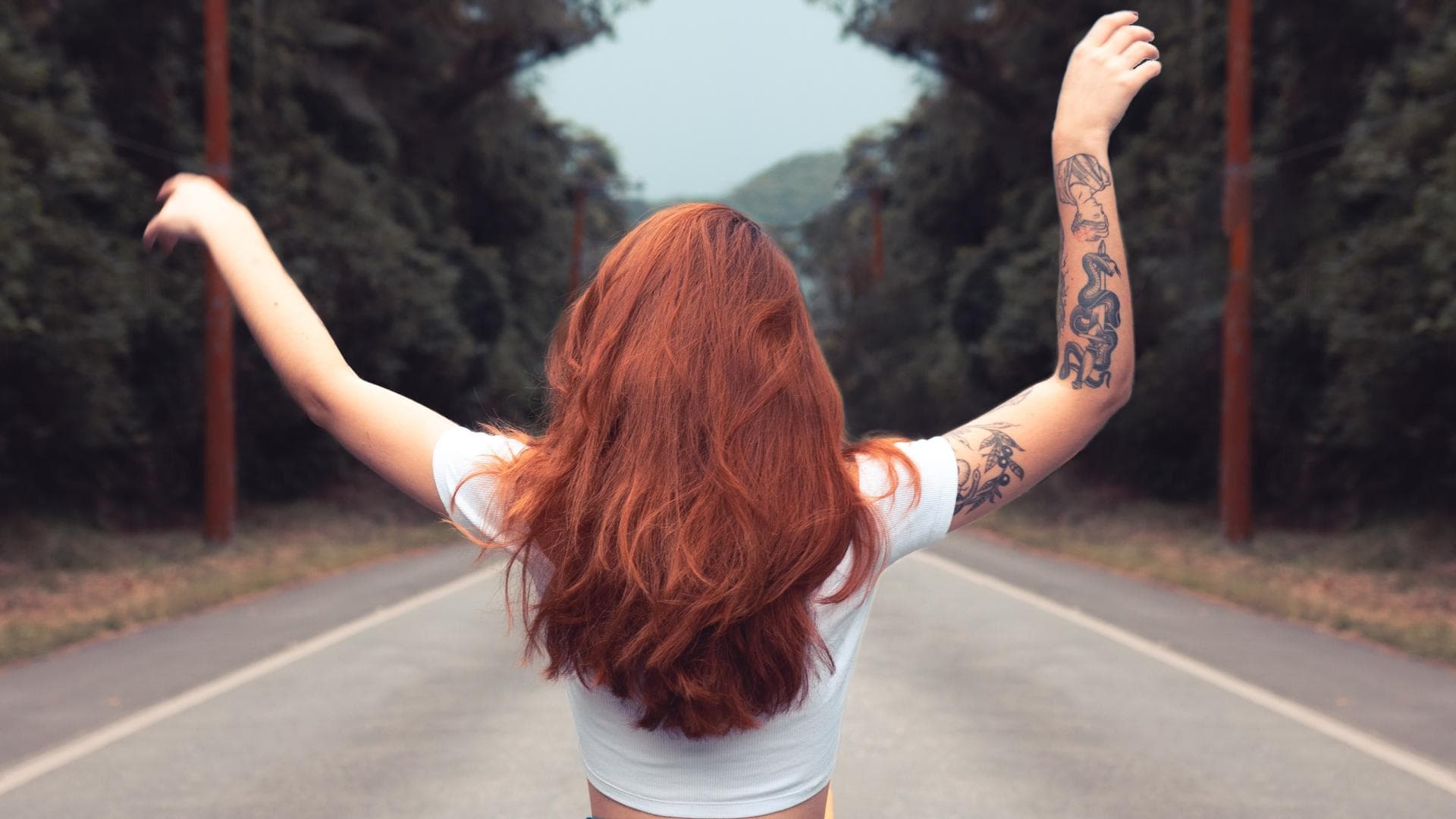 Rothaarige Frau auf einer Straße im Wald mit Tattoos am rechten Arm