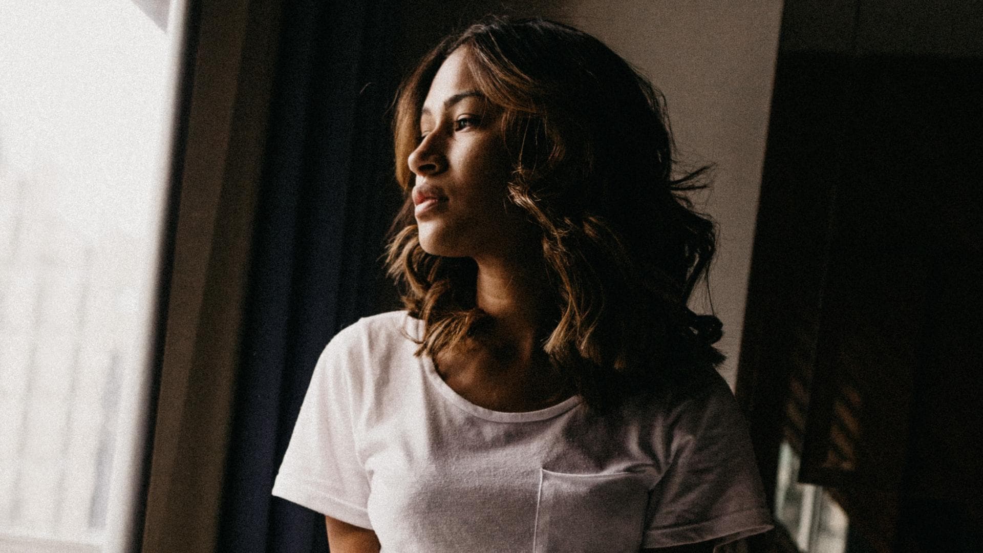 Mädchen kniet auf Bett vor Fenster