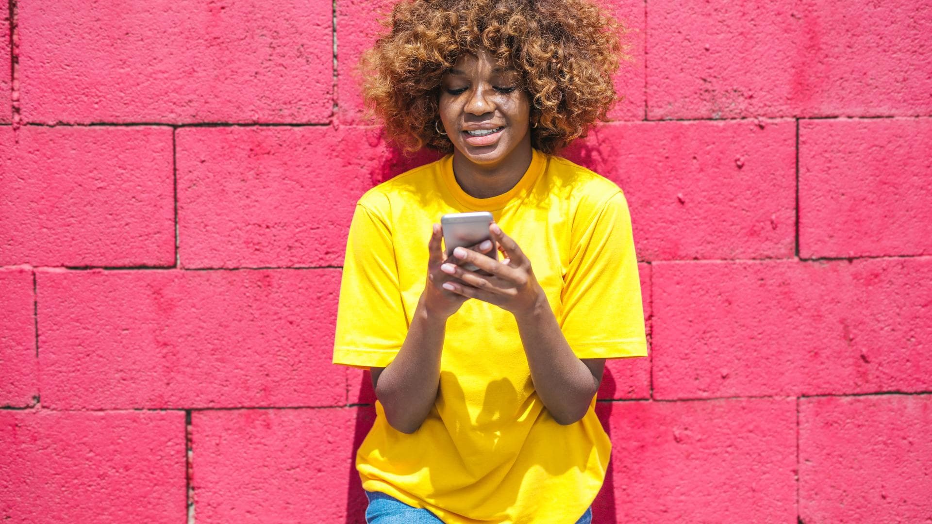 Frau mit Handy steht vor Wand in Pink