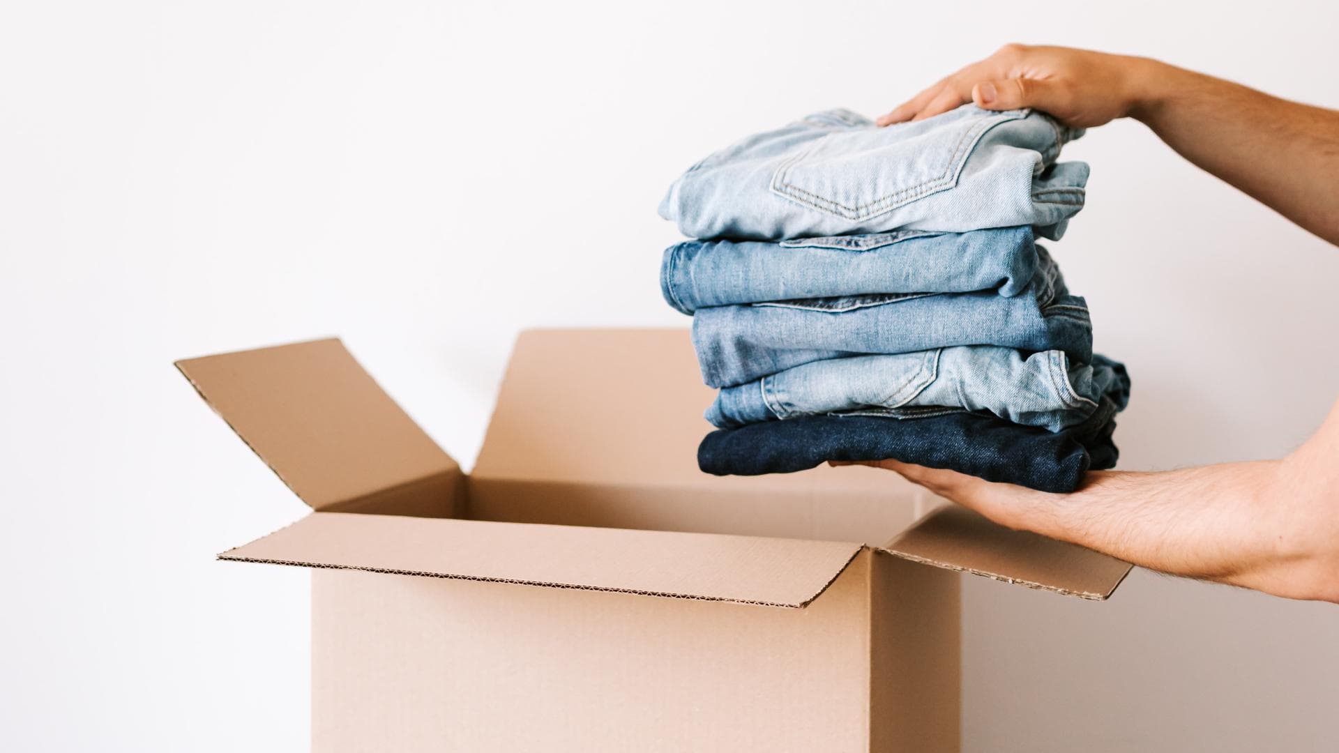 Zwei Hände, die Hosen in einen Karton legen