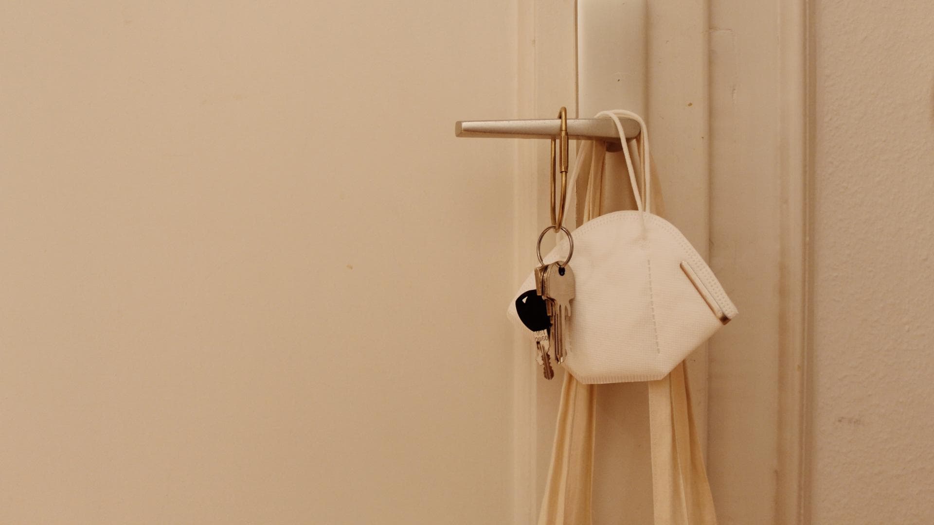 FFP2-Maske hängt an einer Türklinke, davor hängt ein Schlüsselbund
