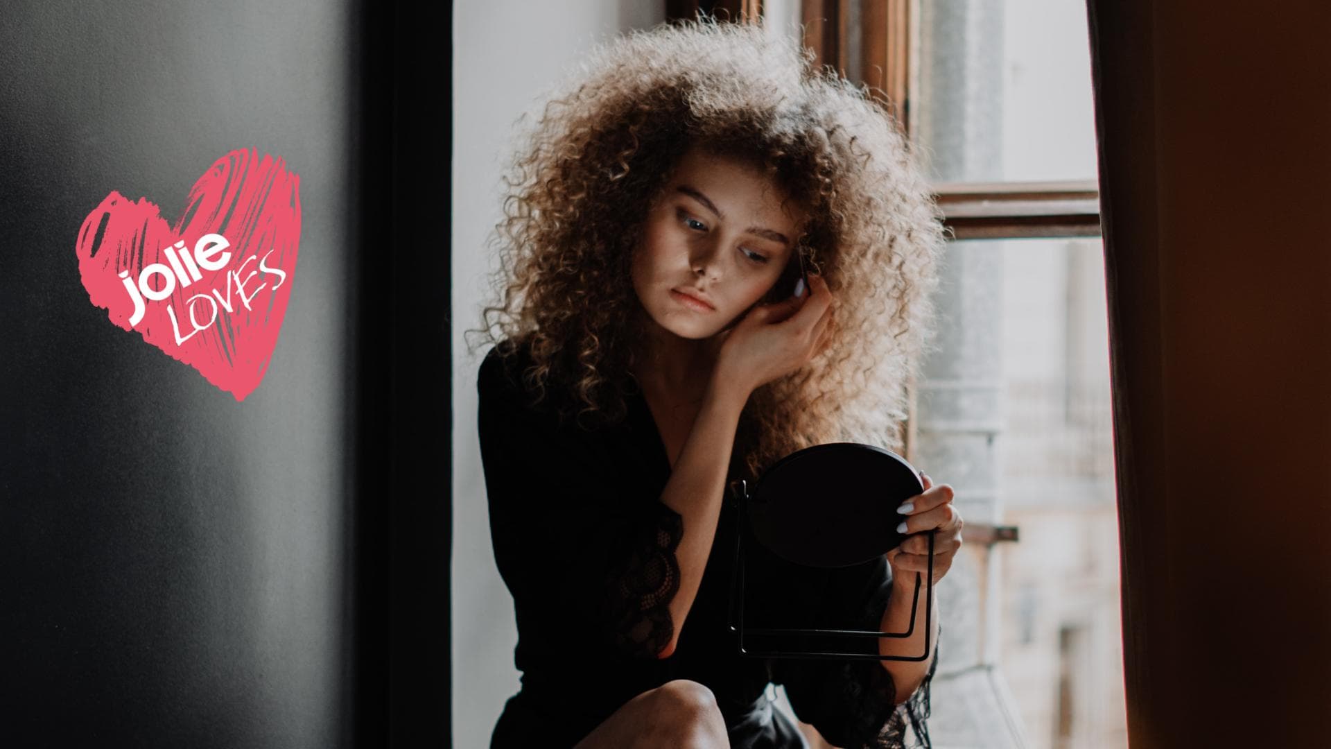 Frau sitzt auf Fensterbank mit Schminkspiegel