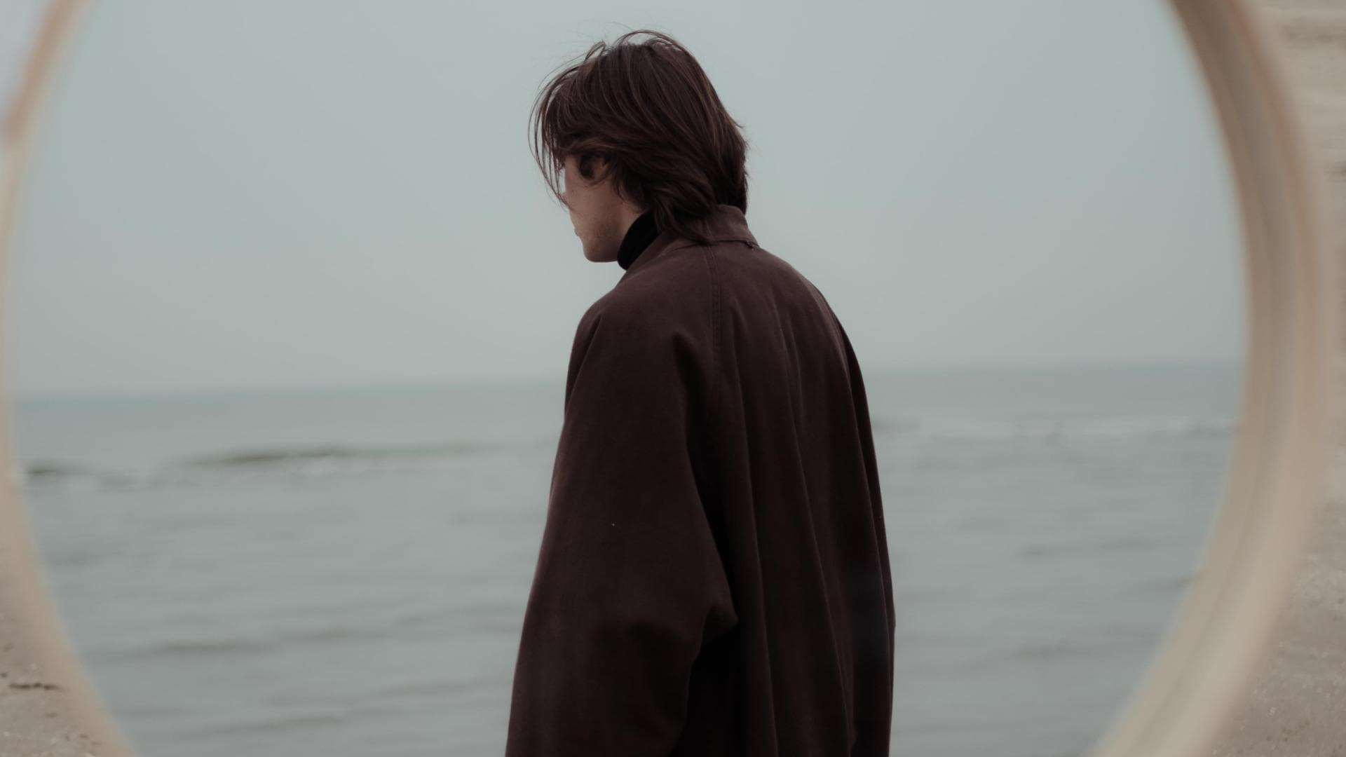 Spiegel am Strand und ein Mann im braunen Mantel ist darin zu sehen