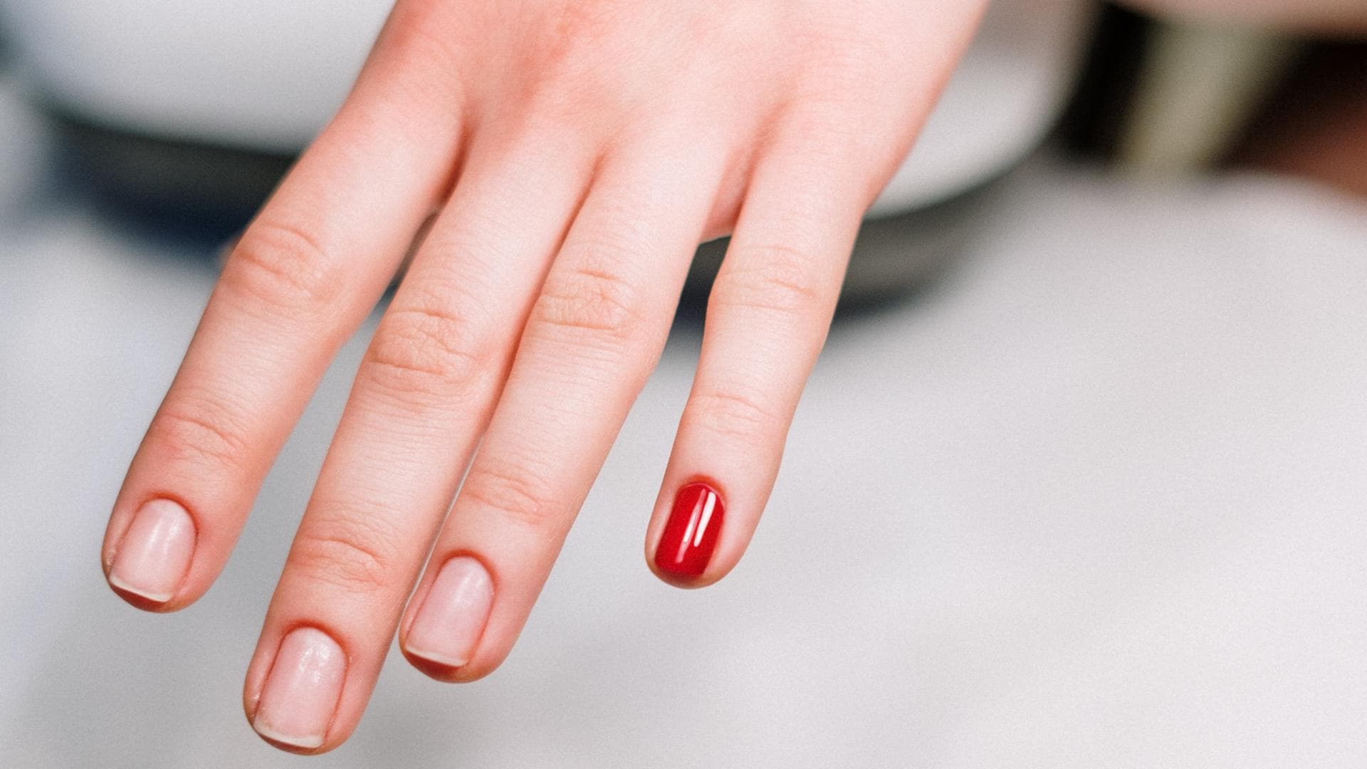 Hand mit natürlichen Nägeln und rotem Nagellack auf dem kleinen Finger