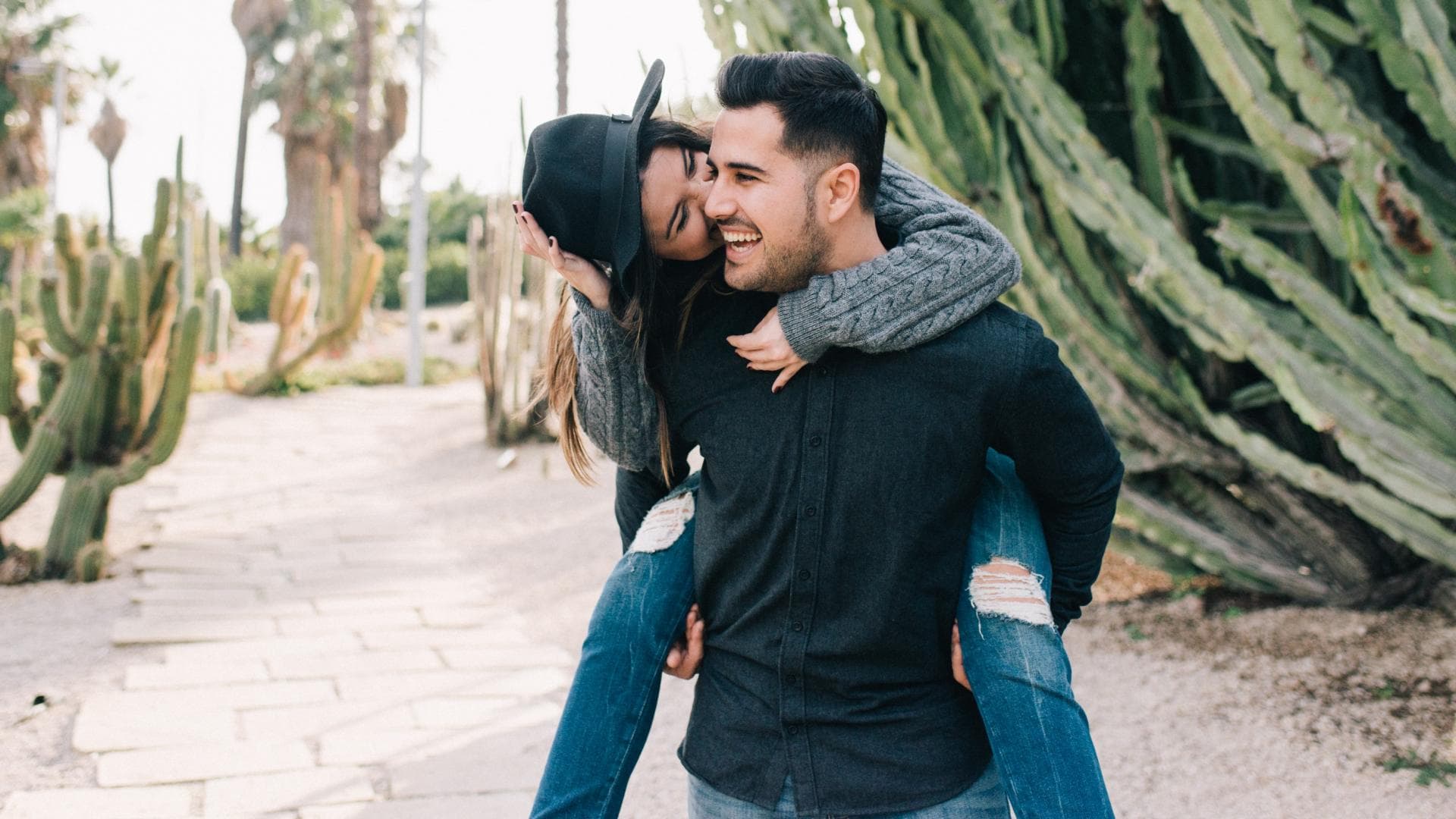 Mann trägt Frau auf dem Rücken, im Hintergrund riesige Kakteen