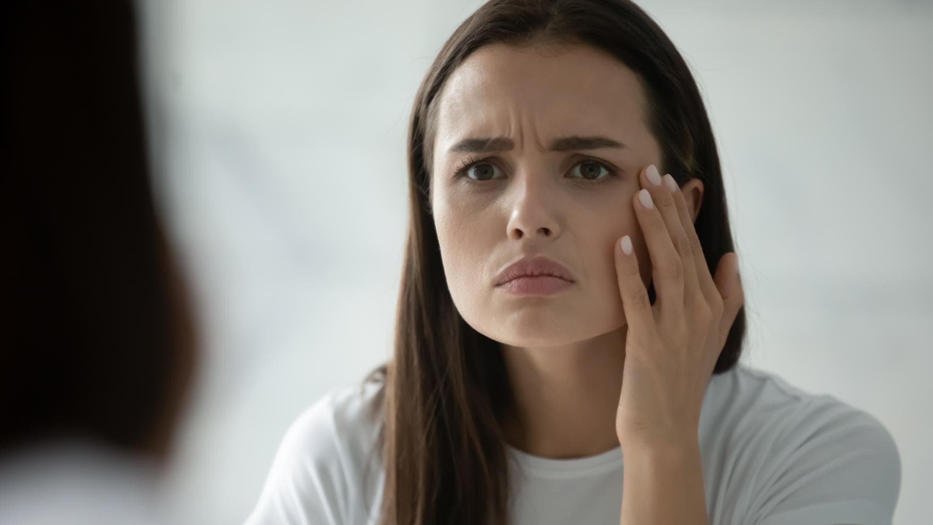 Stirnfalten: Frau steht vor dem Spiegel und runzelt die Stirn