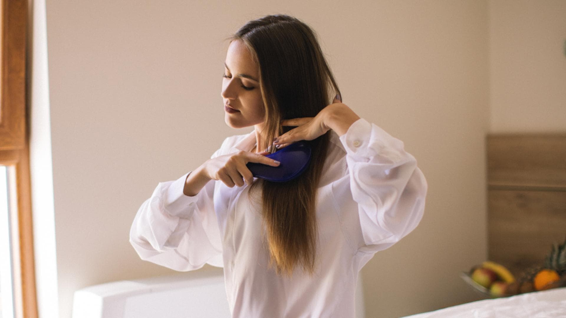 Haare kämmen: Frau sitzt auf einem Bett und bürstet die Haare