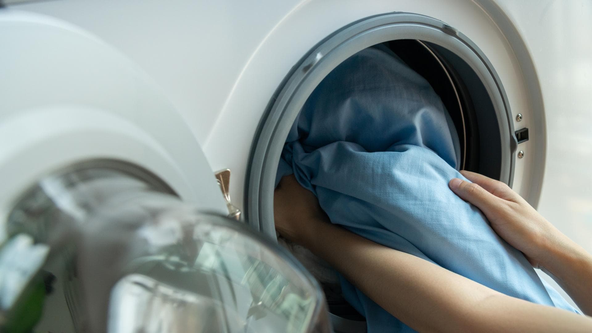 Bettwäsche waschen: Hände packen blaue Bettbezüge in eine Waschmaschine