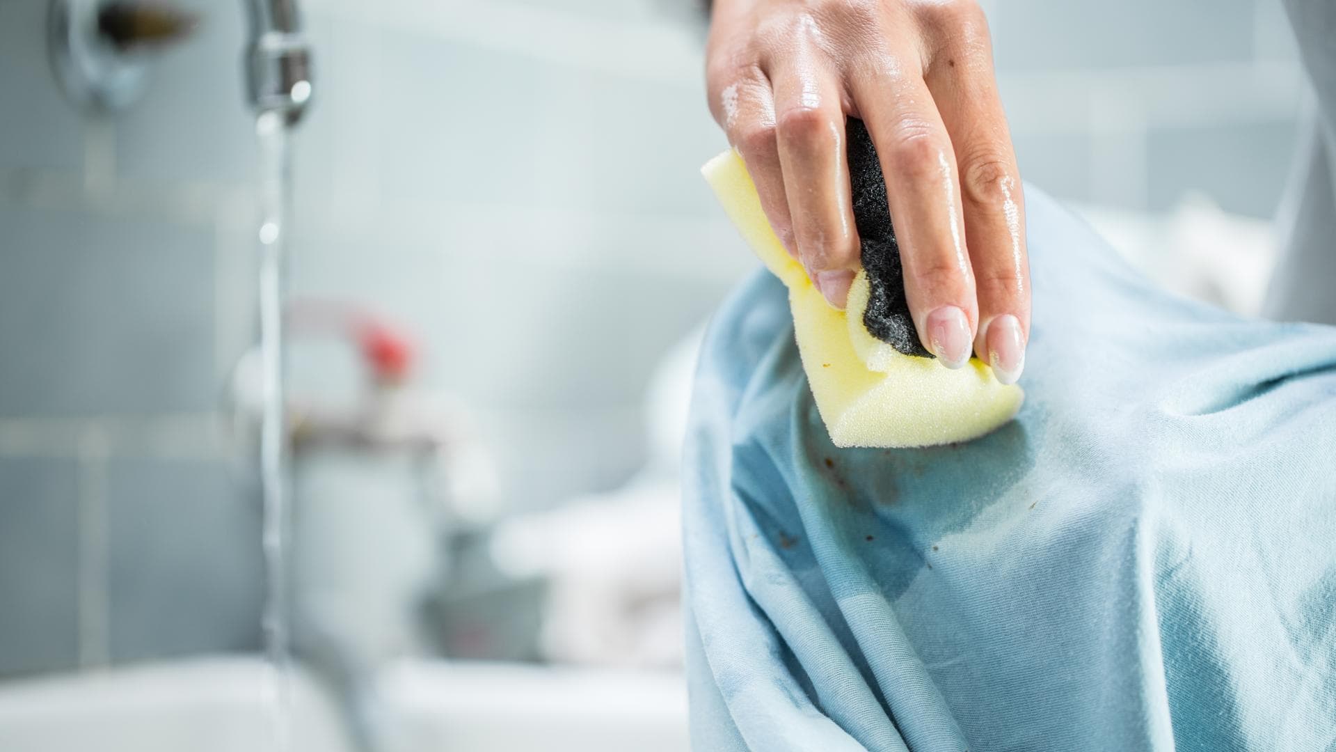 Fettflecken entfernen: Hand wäscht Fleck mit Schwamm aus Kleidungsstück