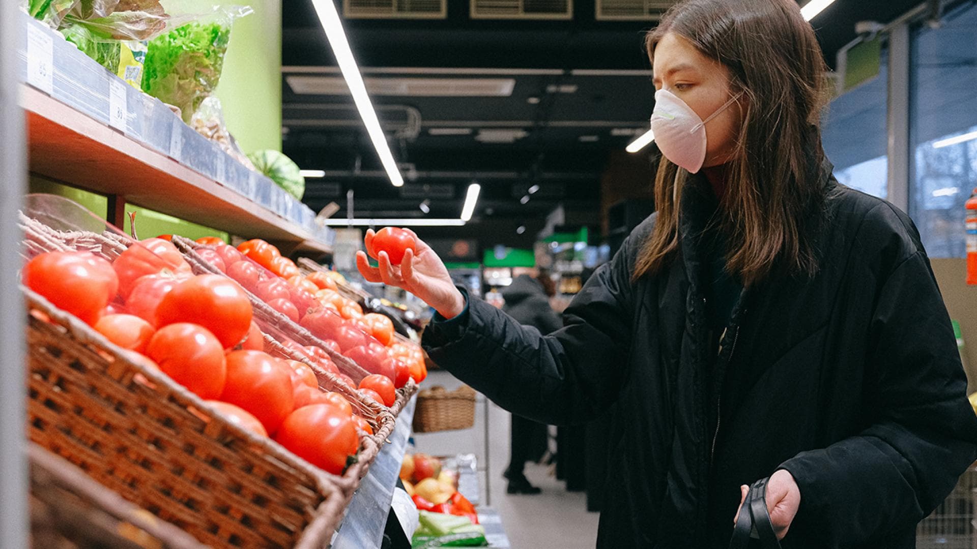 Frau haelt Tomate im Supermarkt