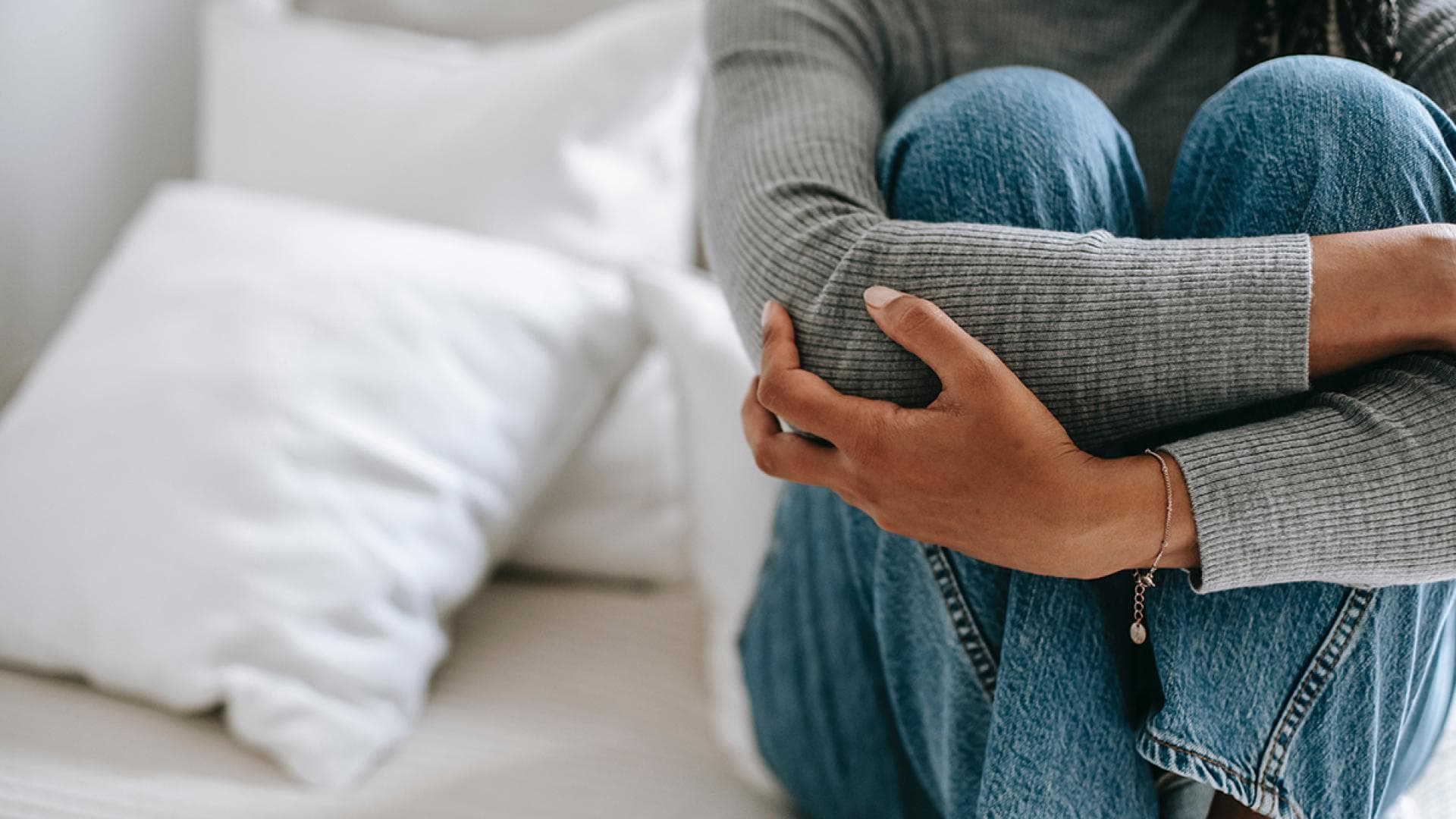 Frau sitzt auf Bett und umschlingt ihre Beine