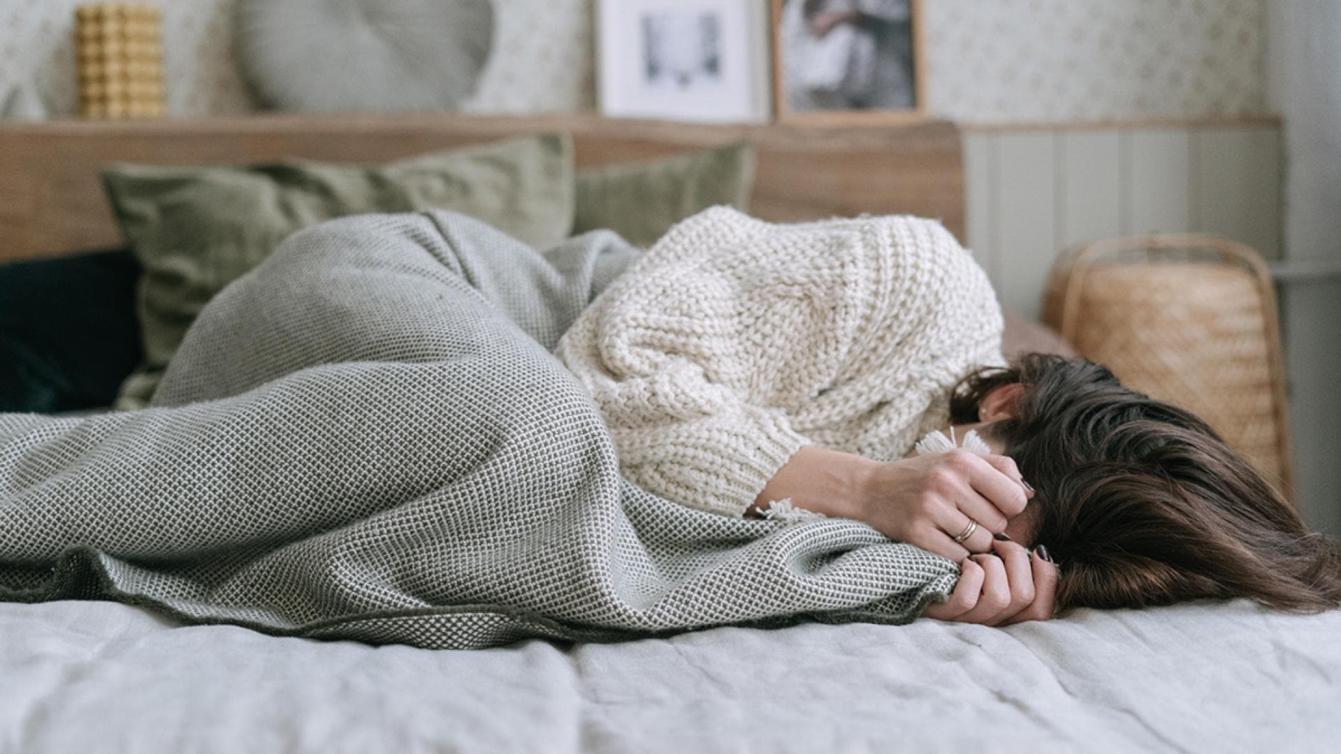 Frau im Bett mit Händen vor Gesicht 