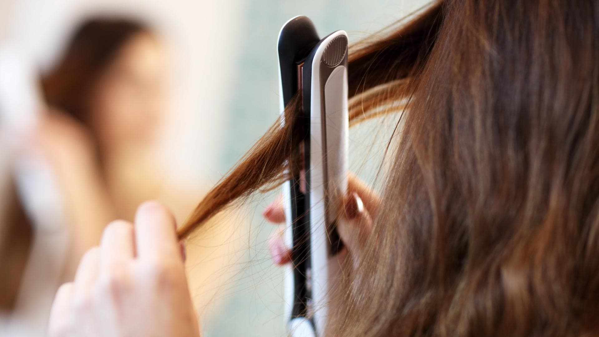 Frau glättet sich die Haare mit Dampfglätteisen