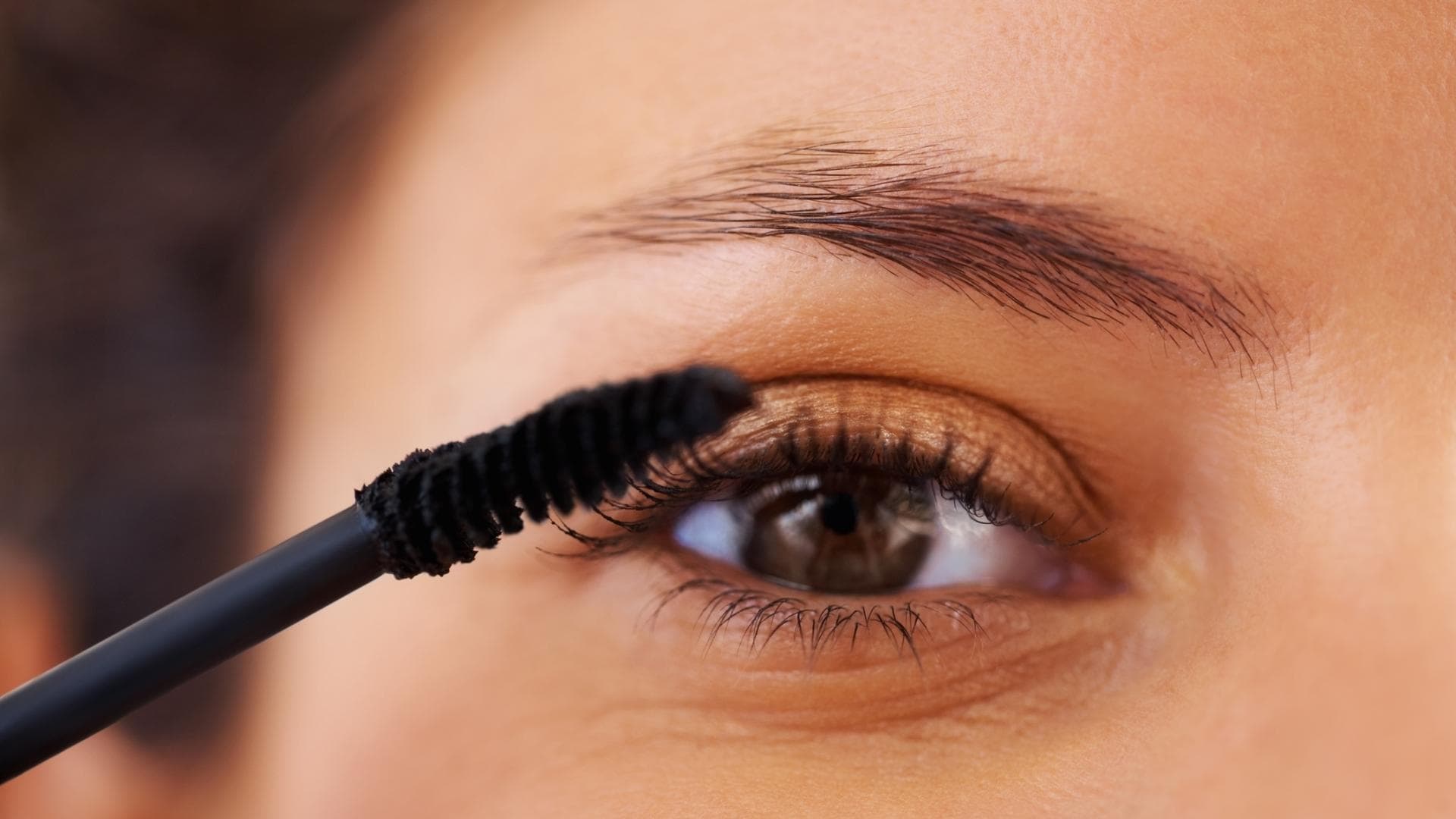 Frau trägt Mascara auf mit braunen Augen