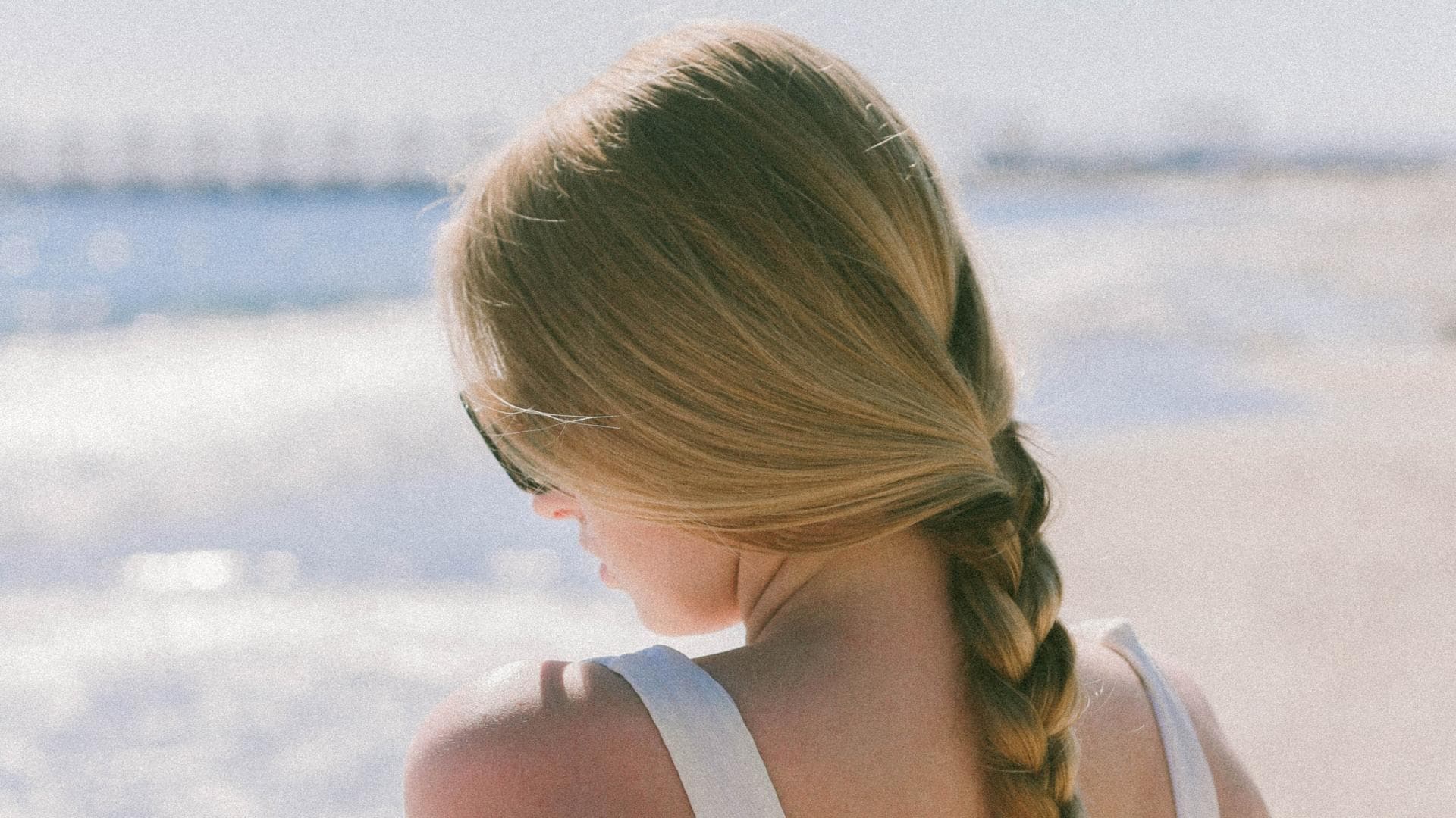 Frau mit geflochtenen Haaren sitzt am Strand