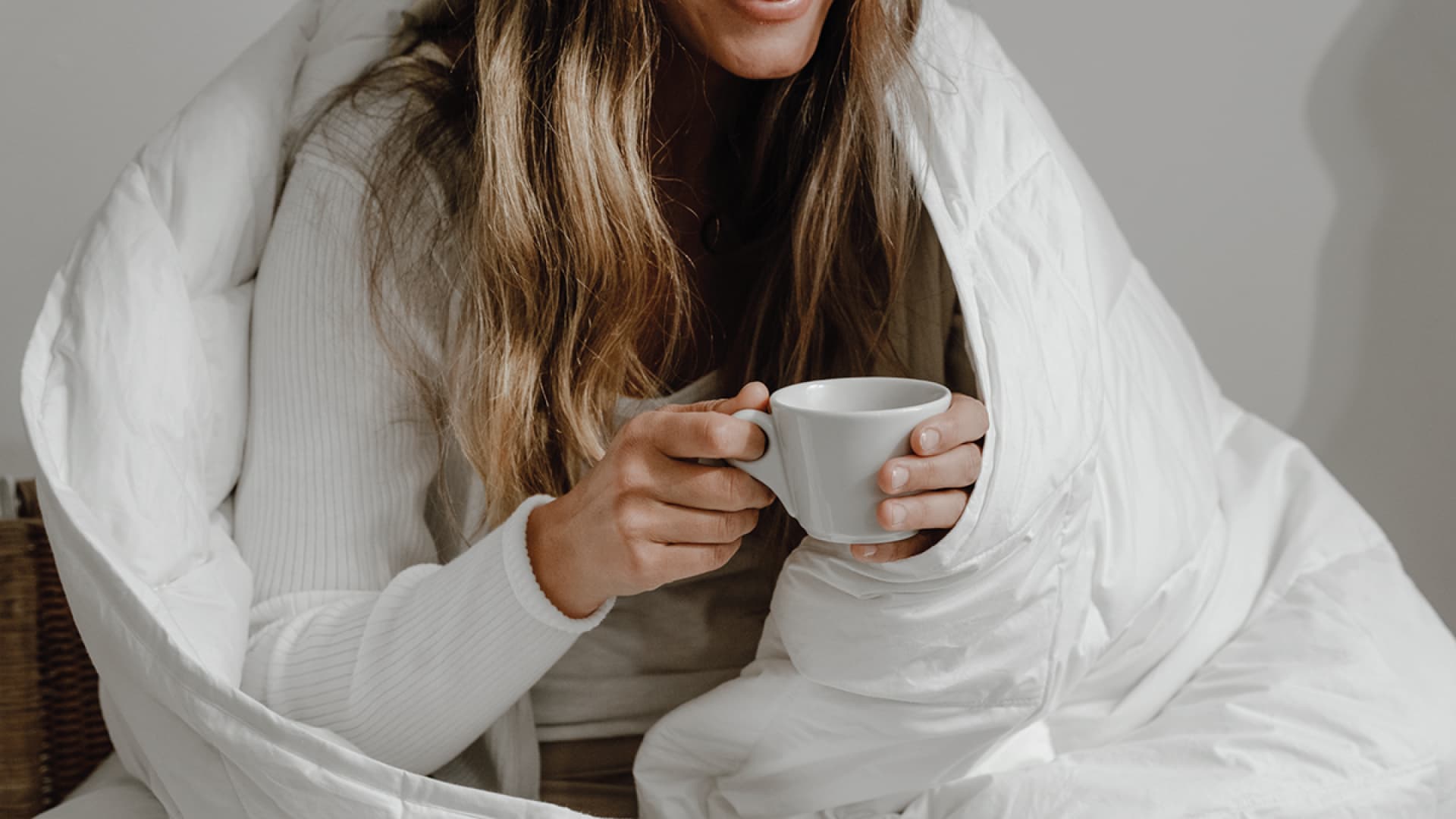 Frau mit Tasse im Bett mit Decke
