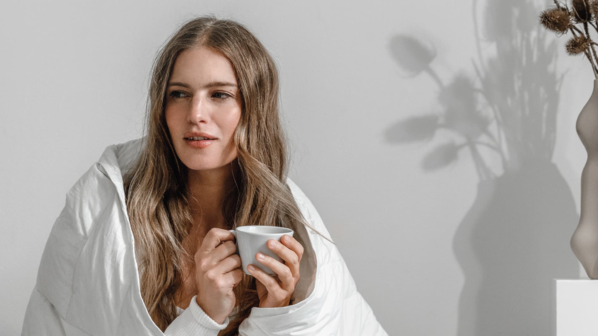Frau hält Tasse in der Hand und trägt eine Decke