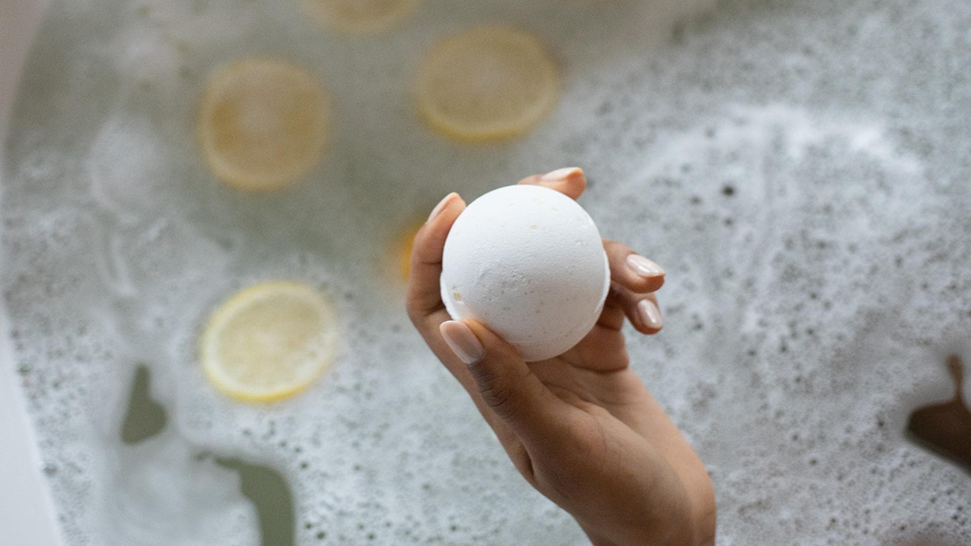 Frau hält Badekugel in der Badewanne