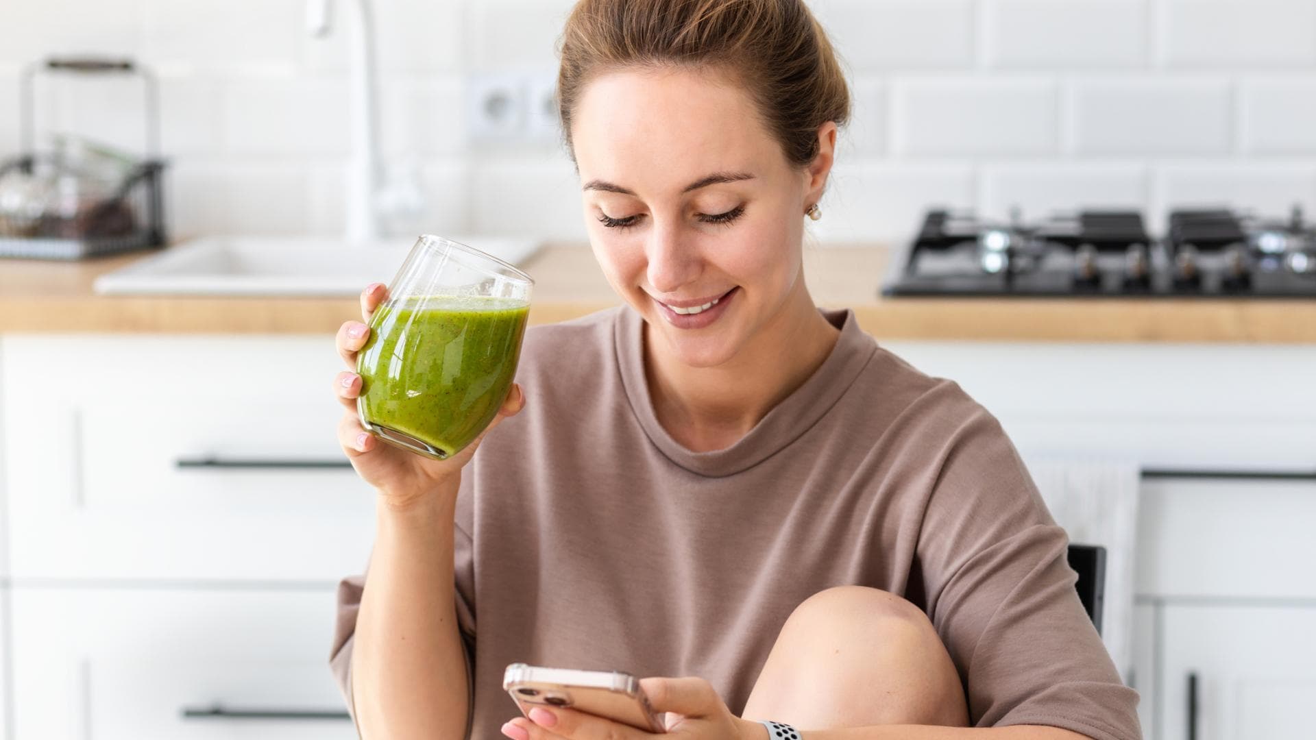 Frau mit grünem Saft schaut auf Handy