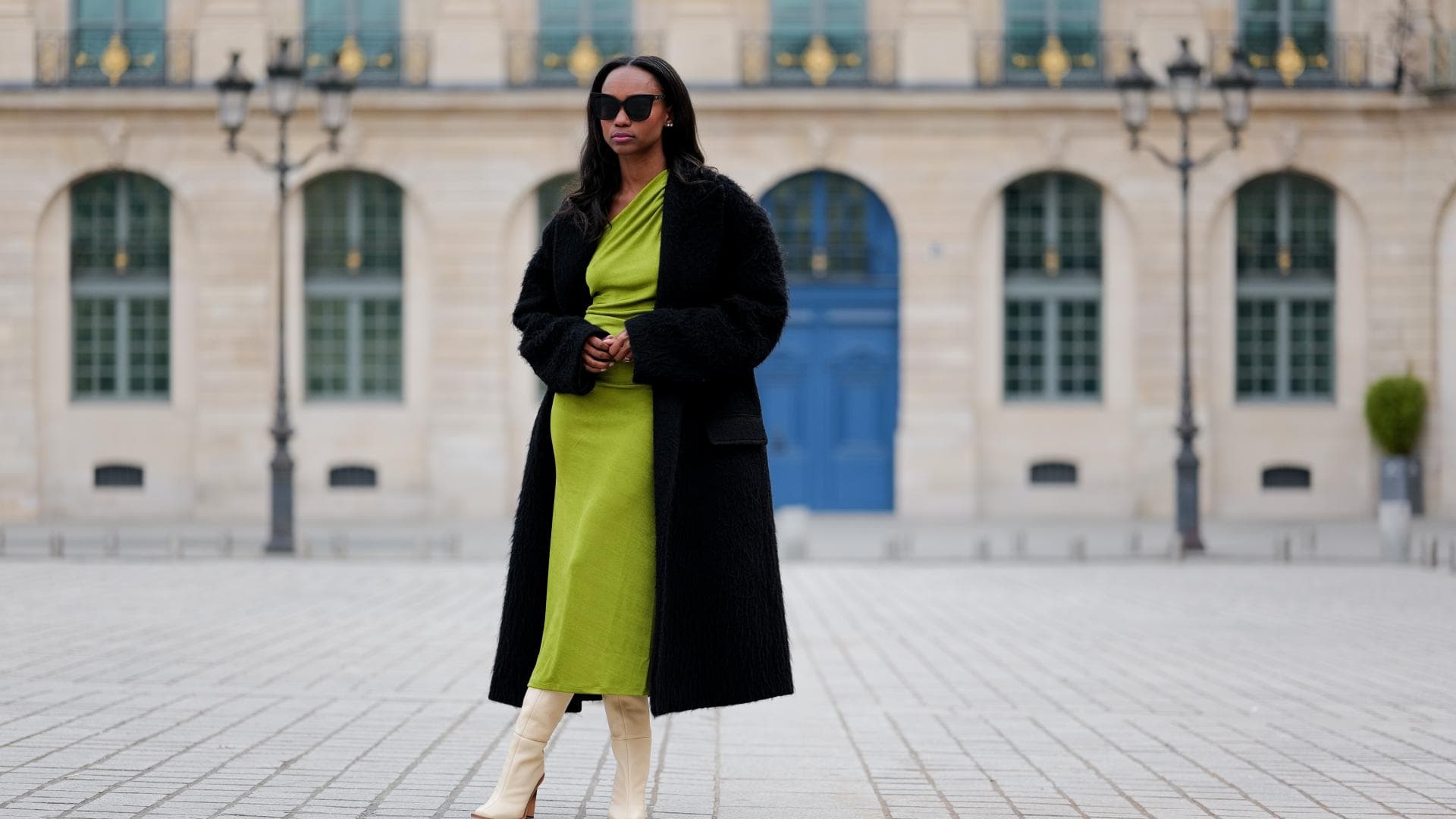 Frau trägt grünes Midikleid aus Satin mit schwarzem Mantel und Stiefeln