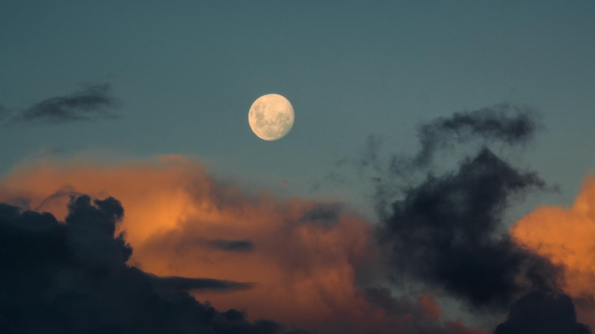 Vollmond am blauen Himmel mit orangefarbenen Wolken