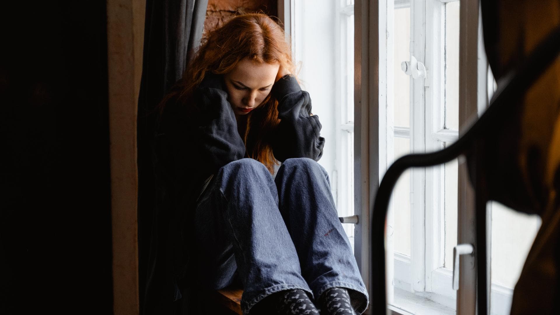 Traurige Frau sitzt auf einer Fensterbank