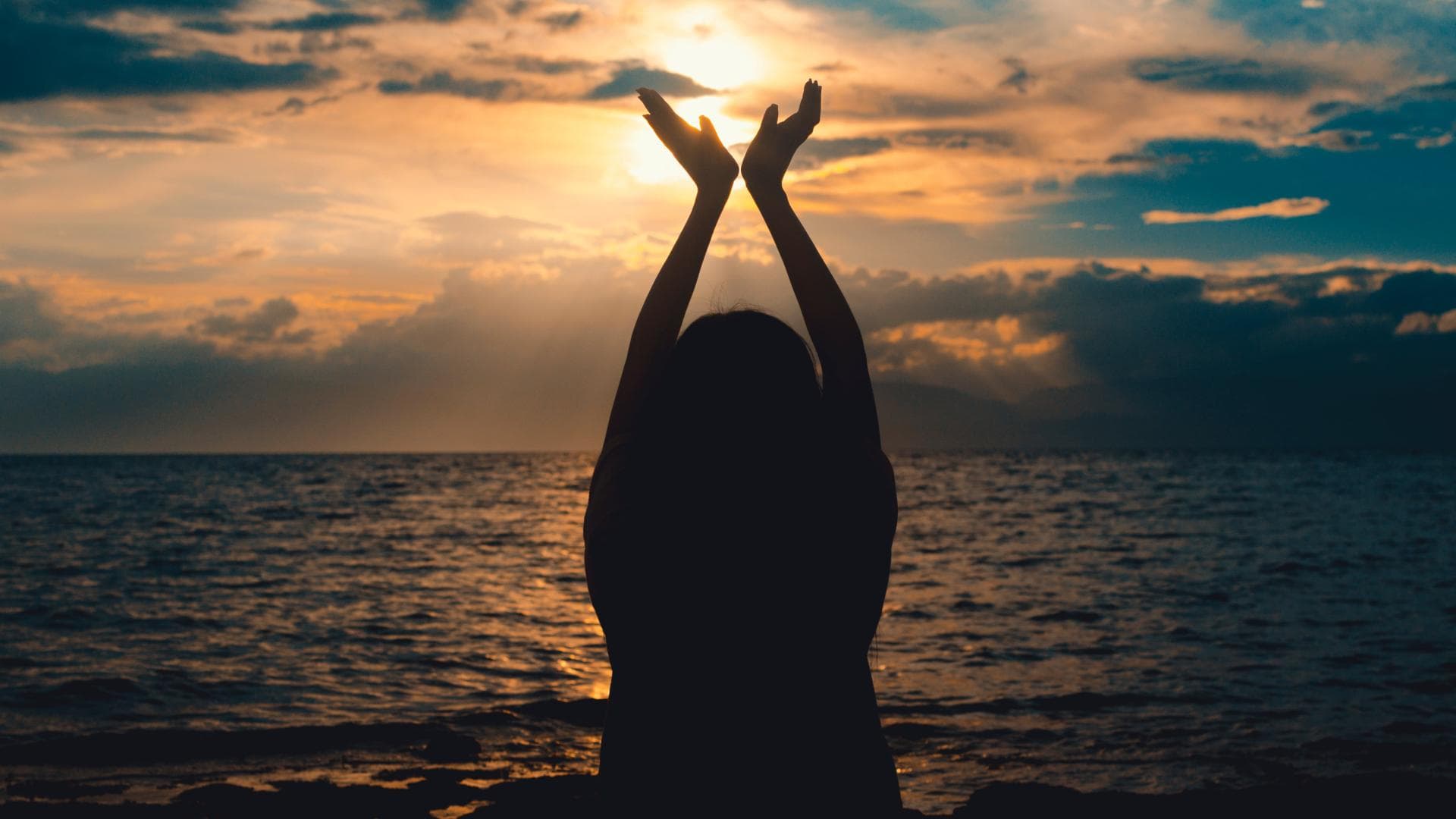 Frau am Meer, die ihre Hände in die Luft streckt