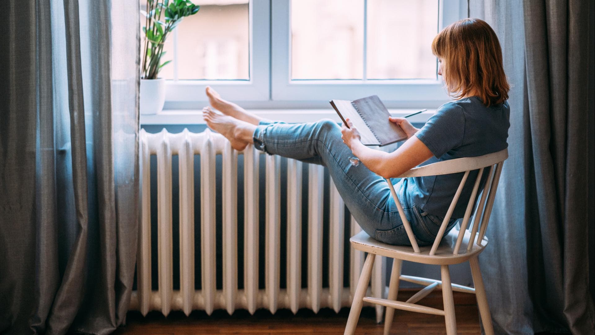 Frau die vor einer Heizung sitzt