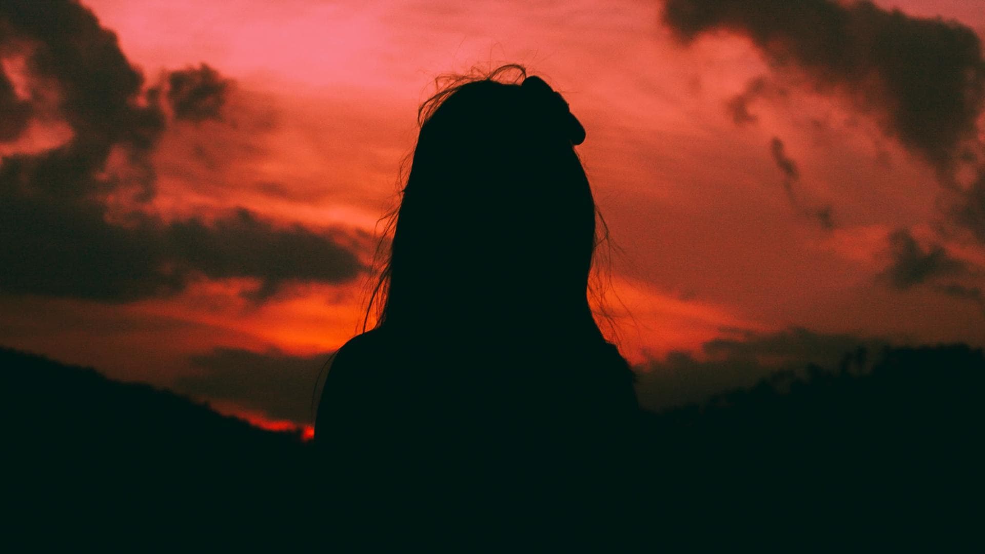 Silhouette einer Frau mit langen Haaren vor einem orange-rosafarbenen Himmel
