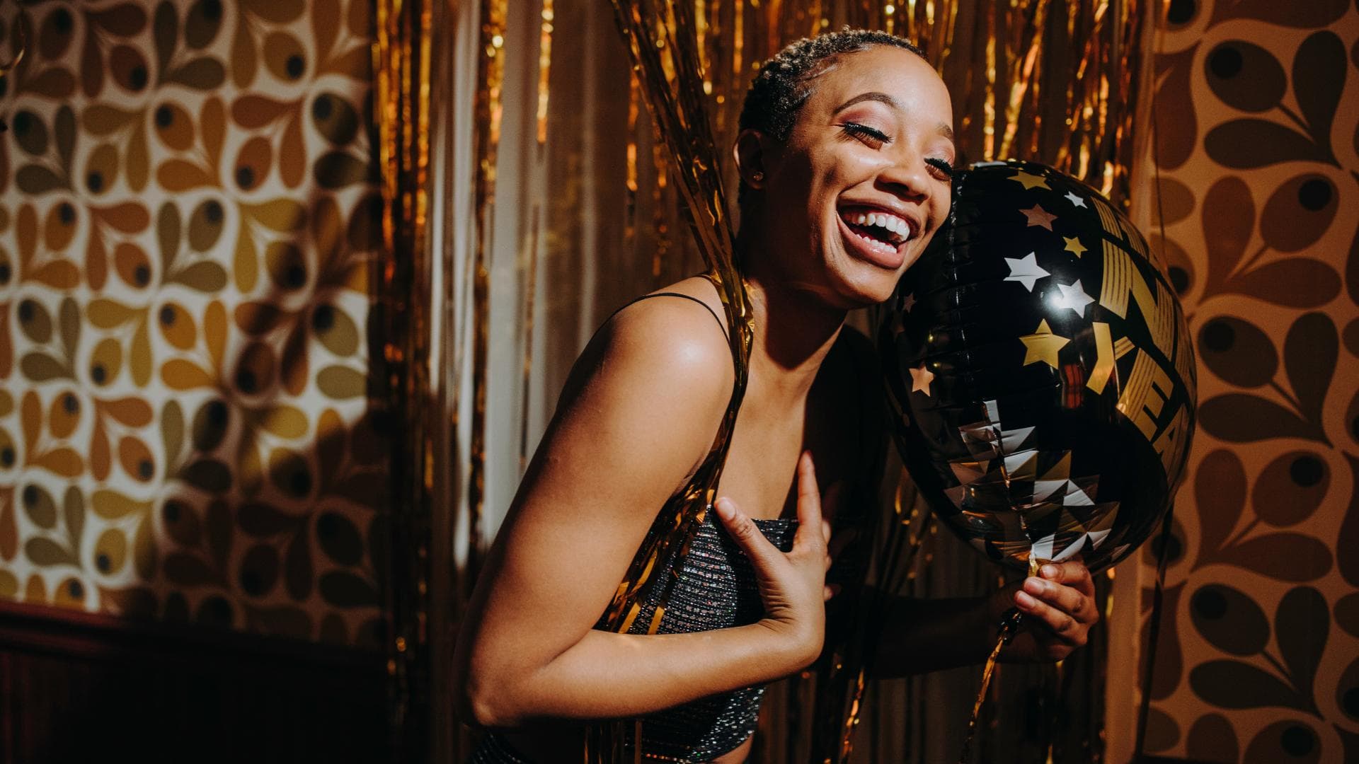 Glückliche Frau hält einen schwarzen Luftballon mit der Aufschrift "Happy New Year" in der Hand
