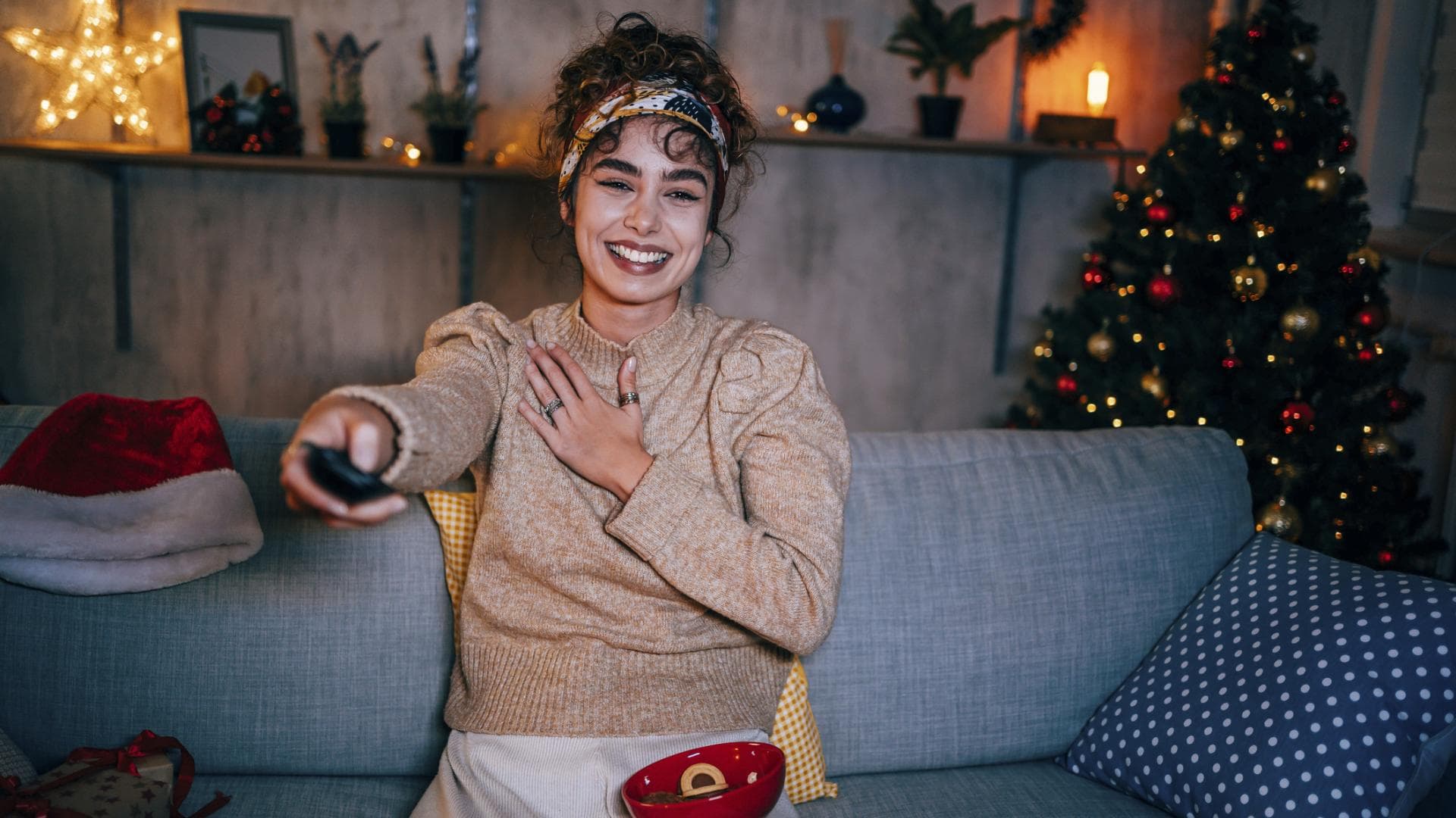 Frau sitzt auf dem Sofa und guckt in ihrer weihnachtlich dekorierten Wohnung Fernsehen