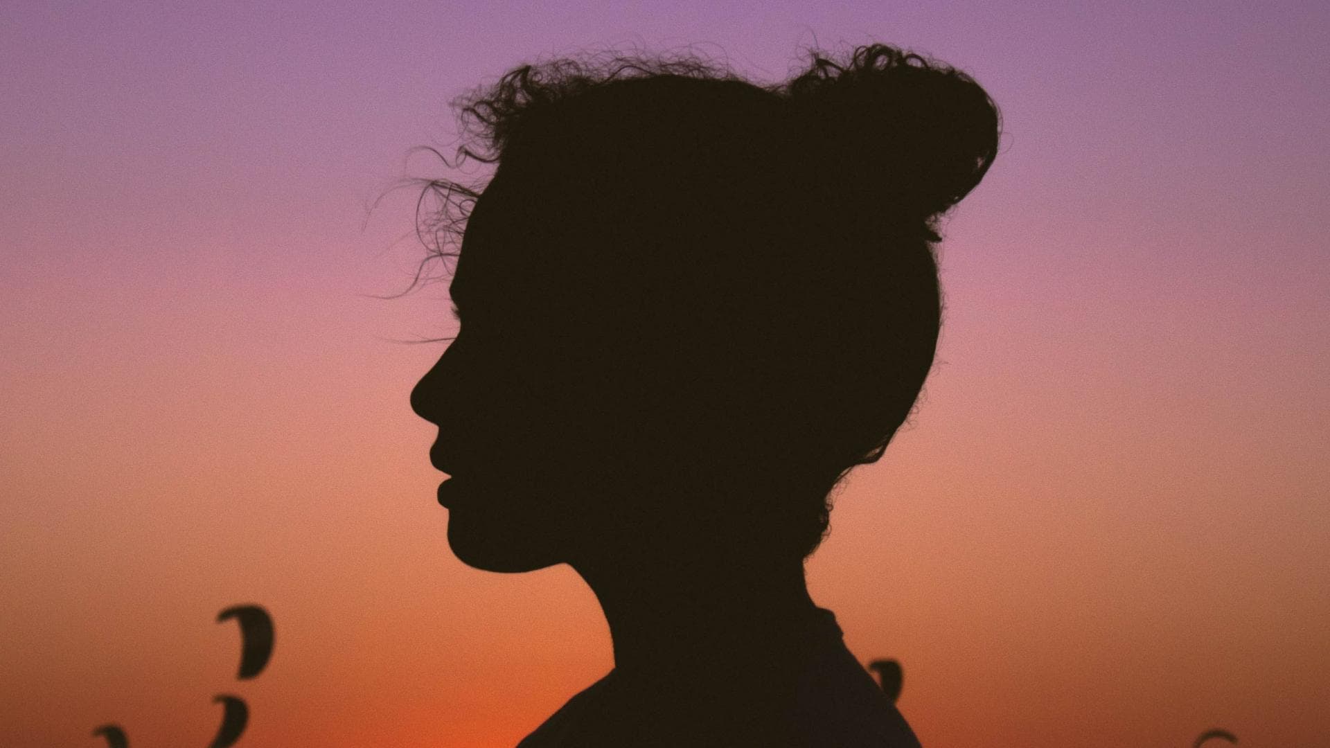 Frau mit Dutt steht vor einem Sonnenuntergang