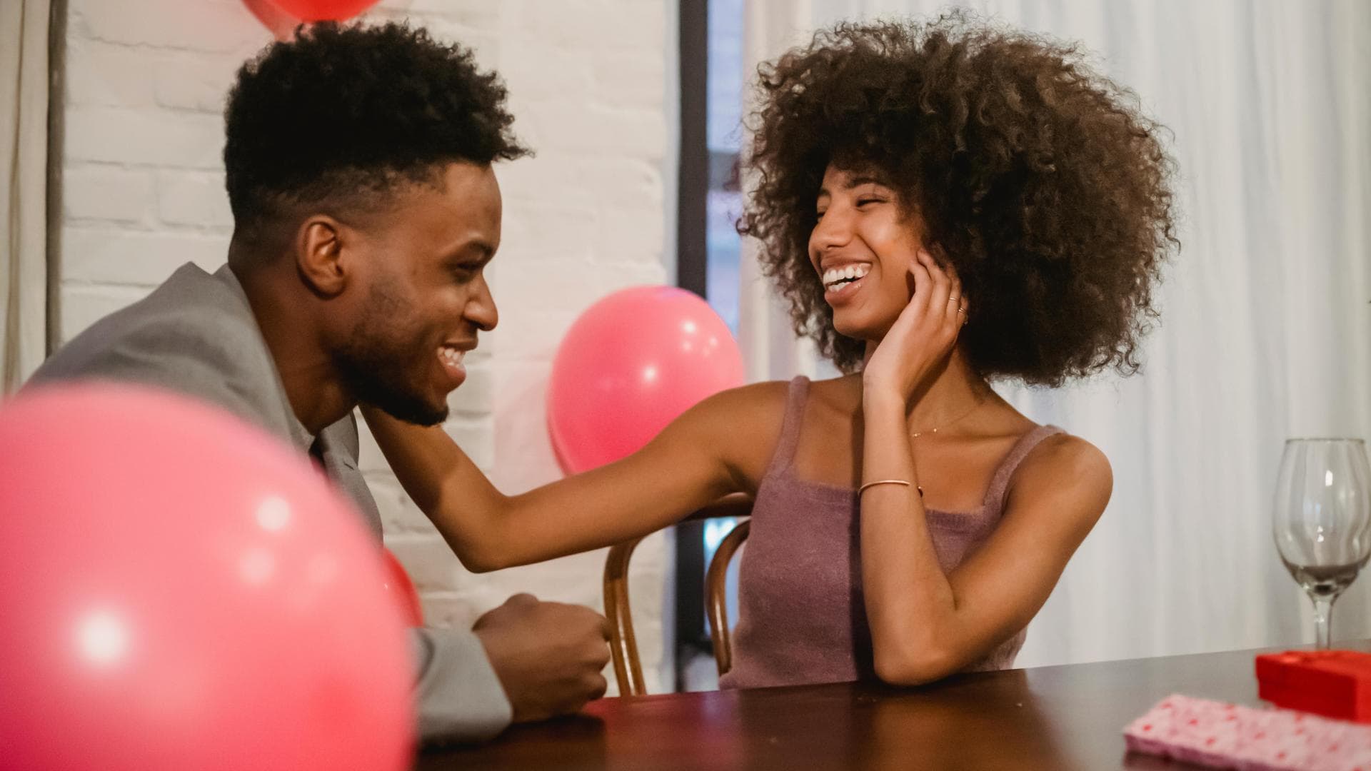 Mann und Frau sitzen am Tisch mit Luftballons und lachen