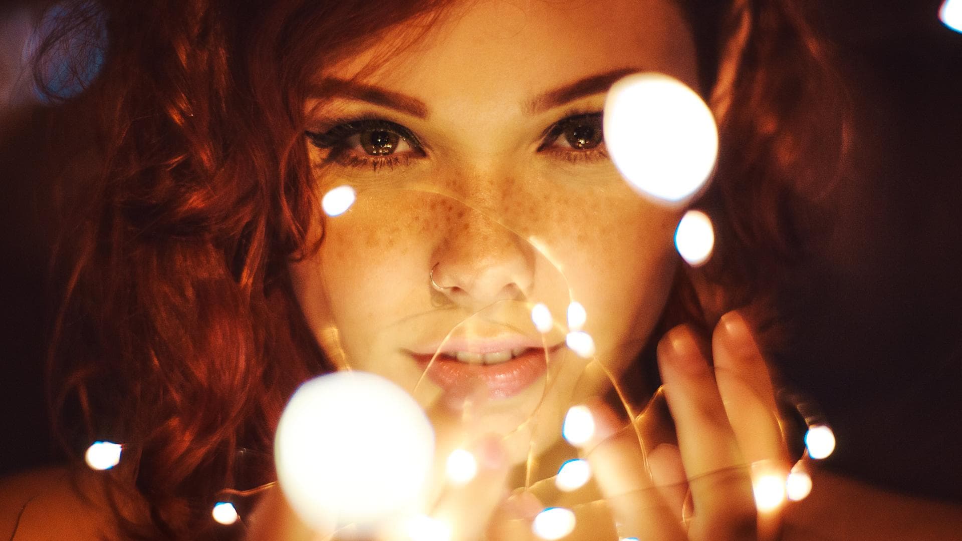 Frau mit Sommersprossen und Eyeliner hält eine Lichterkette in der Hand