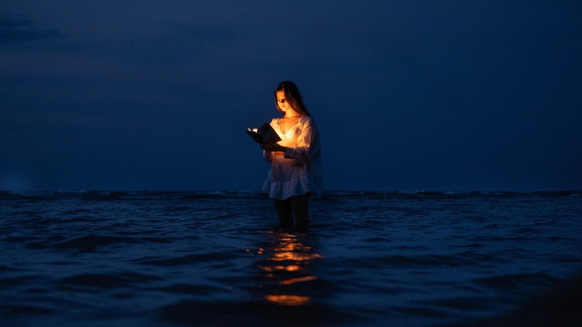 Frau steht im Meer und liest ein Buch