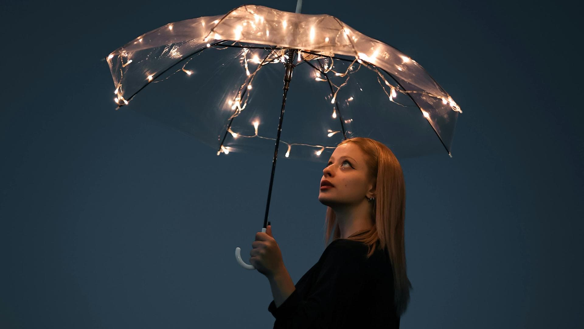 Frau hält einen Regenschirm mit Lichterketten in der Hand