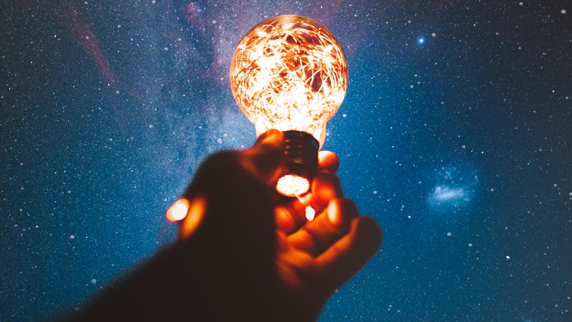 Hand hält eine Glühbirne in den Nachthimmel