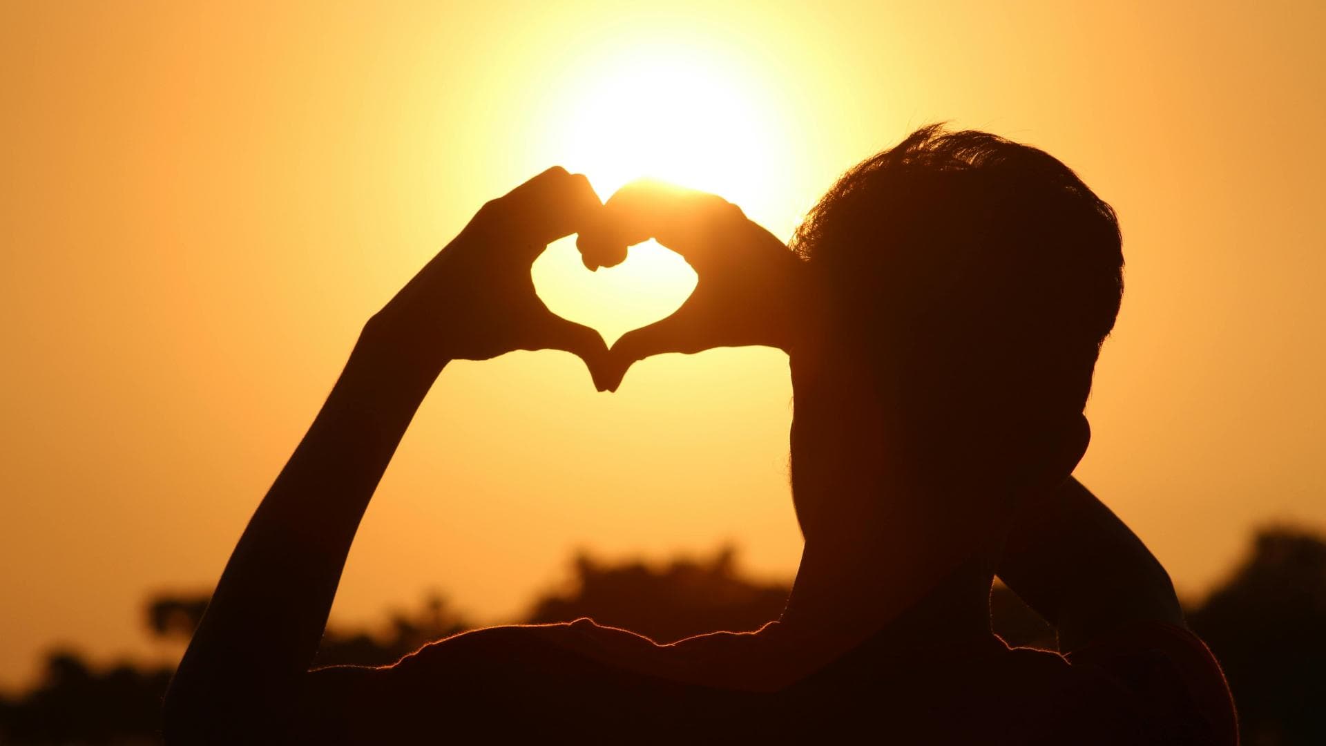 Person zeigt Herz vor Sonne