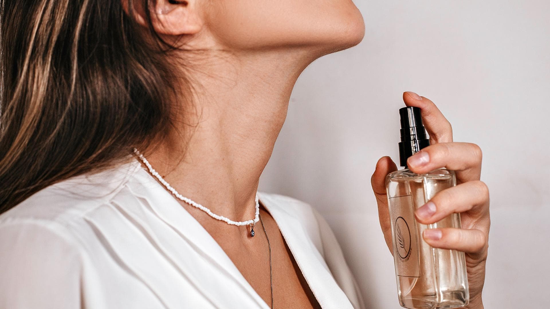 Frau besprüht Hals mit Parfum