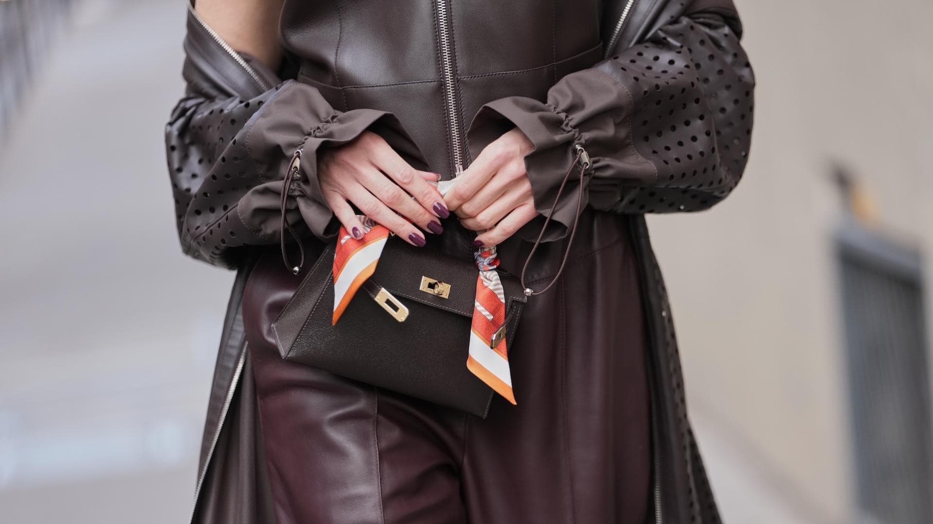 Eine Frau trägt ein braunes Outfit und hält vorn ihre Tasche mit den Fingern fest.