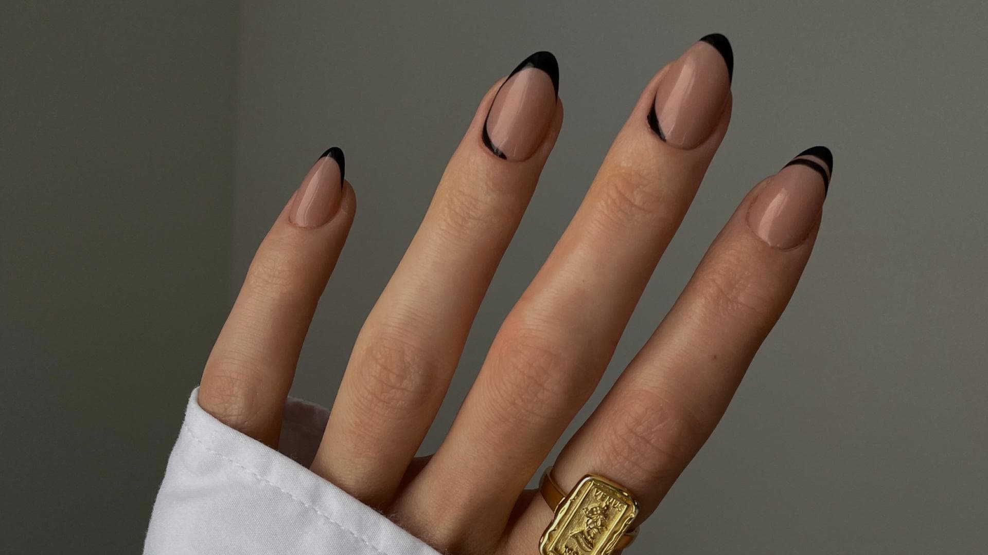 Die Hand einer Frau mit schwarzen schwarzen French Nägeln und einem goldfarbenen Ring am Zeigefinger.