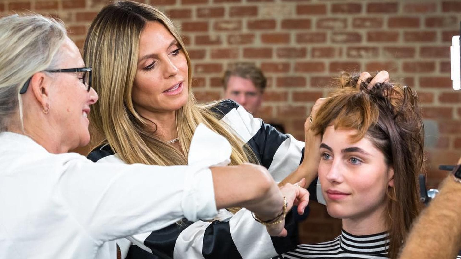 Am Set von Germany's Next Topmodel beim Umstyling steht Heidi Klum mit einer Friseurin bei einer Kandidatin.