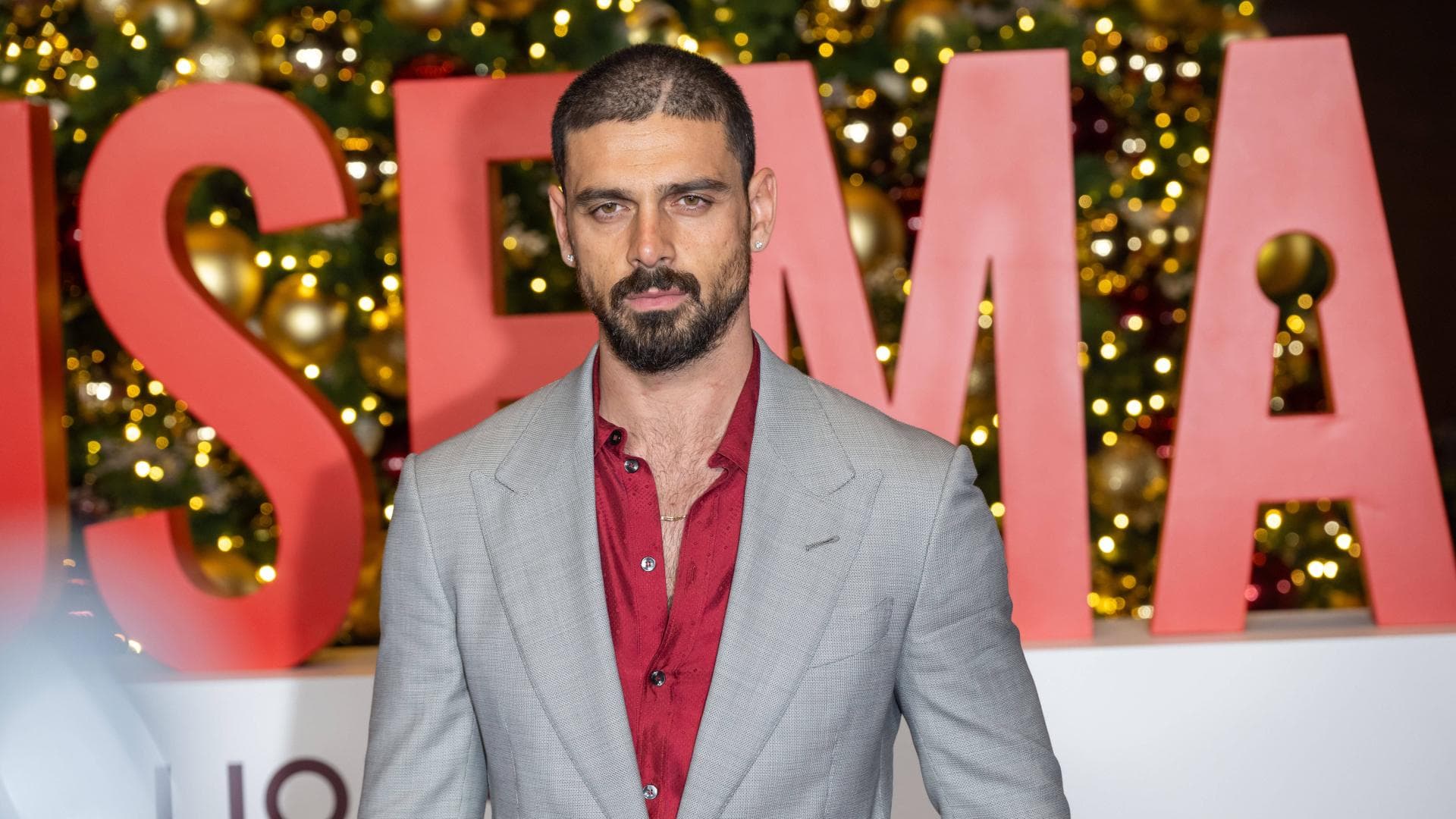 Michele Morrone in einem grauen Anzug mit rotem Hemd darunter.