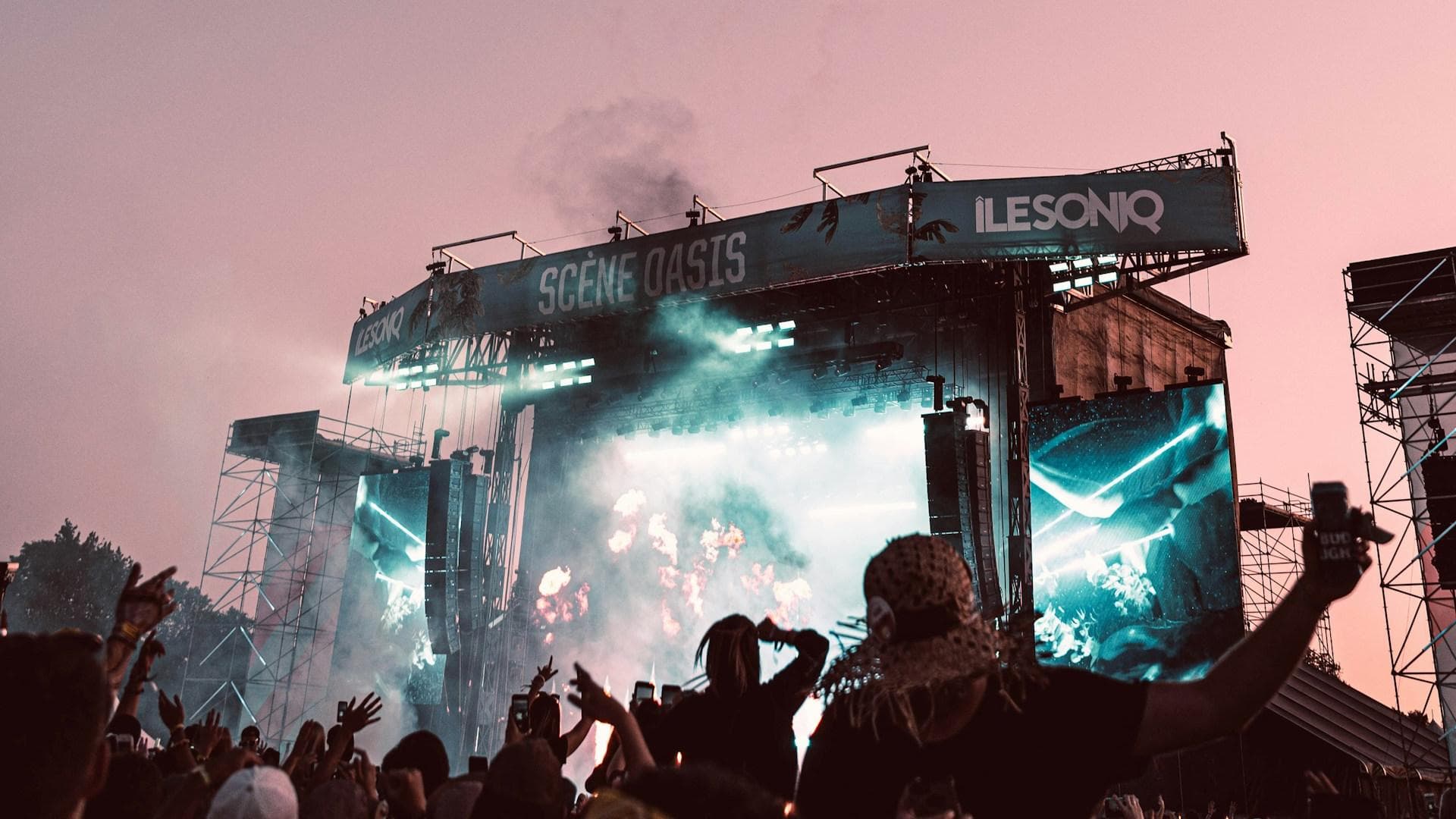 Festival-Bühne bei rosafarbener Dämmerung mit Feuerwerk am Himmel.