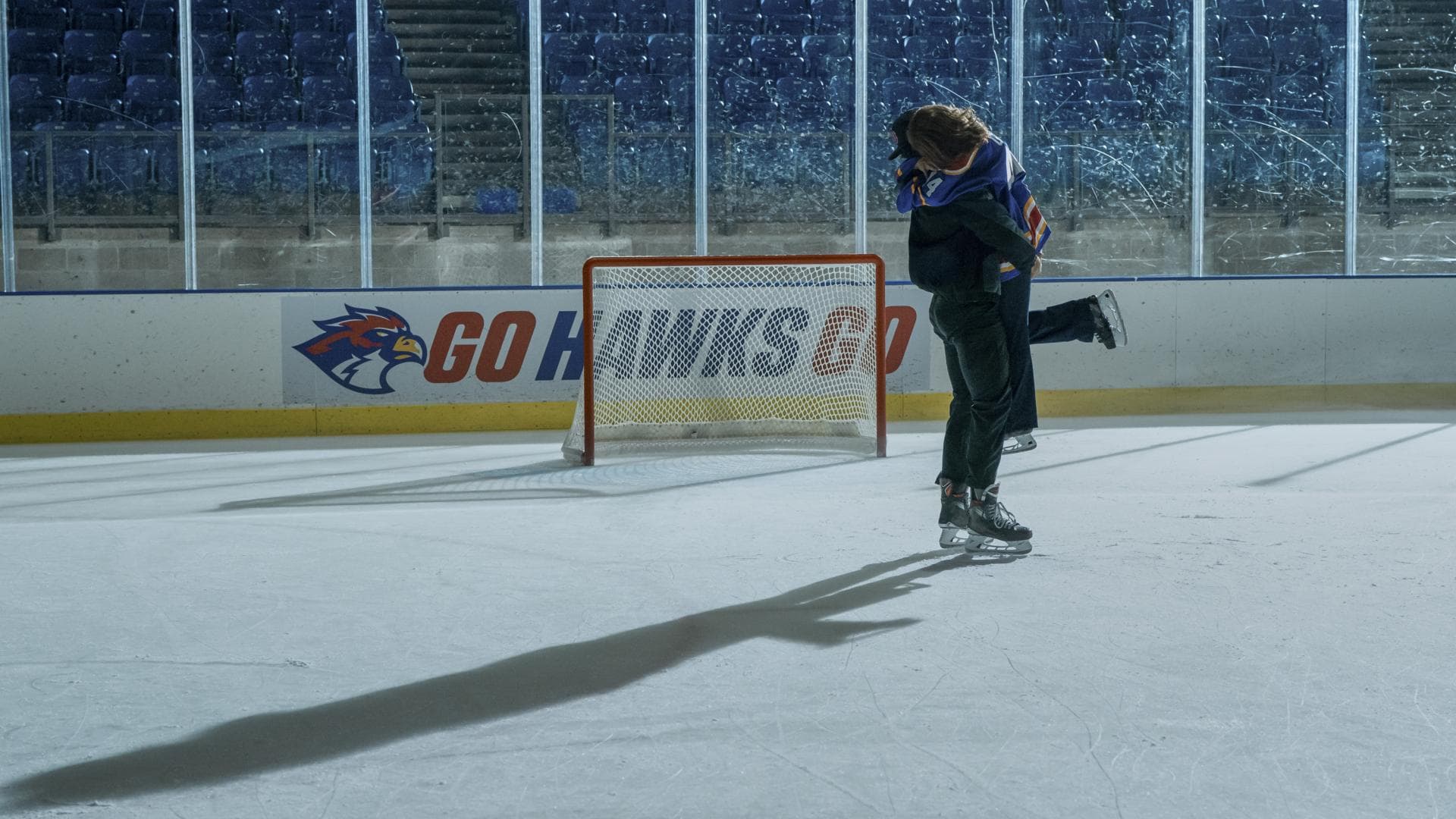 Ein Mann und eine Frau fallen sich auf einem Eishockeyfeld in die Arme.