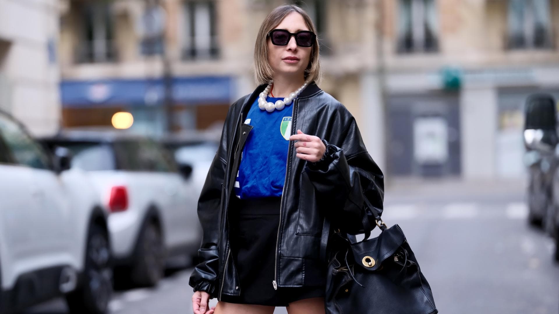 Eine Frau trägt einen schwarzen kurzen Rock, ein Italien Trikot, eine schwarze Lederjacke und eine Sonnenbrille plus Tasche.