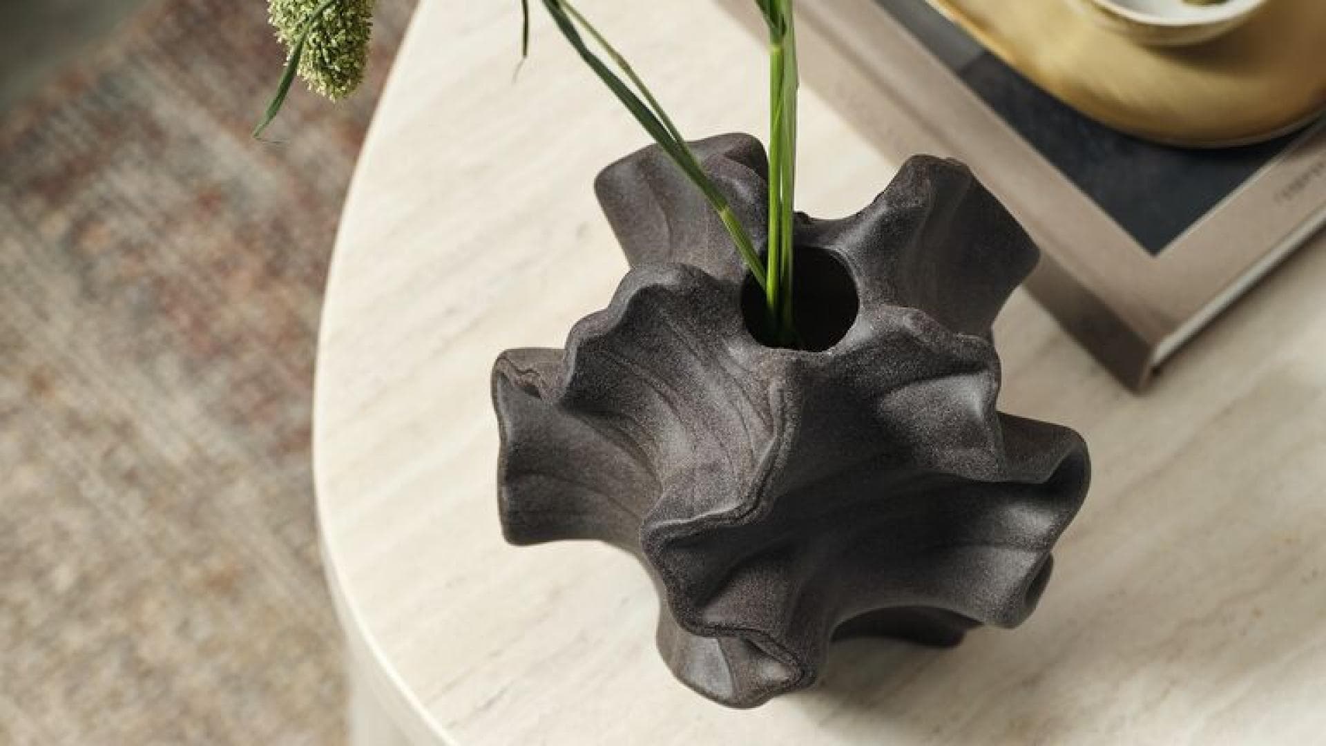 Eine organische Vase mit ein paar Gräsern auf einem Couchtisch von oben betrachtet.