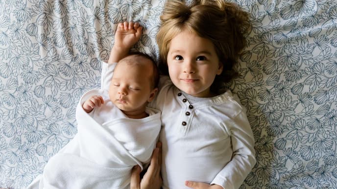 Ein Baby und ein Kleinkind liegen auf einem Bett