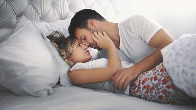 Pärchen liegt im Bett und schaut sich in die Augen