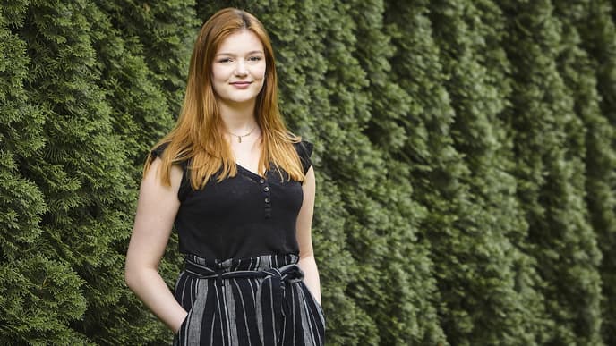 Frau steht vor Hecke